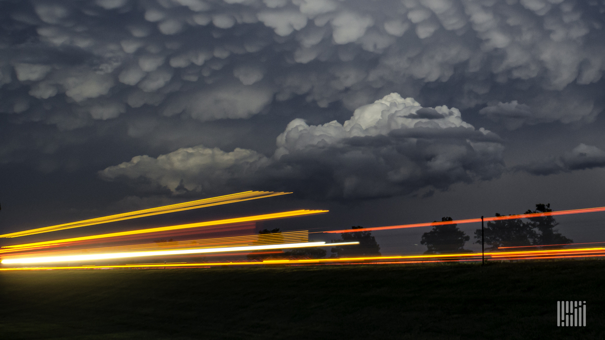 Storm cloud across the sky with vehicle light streaking along the horizon.