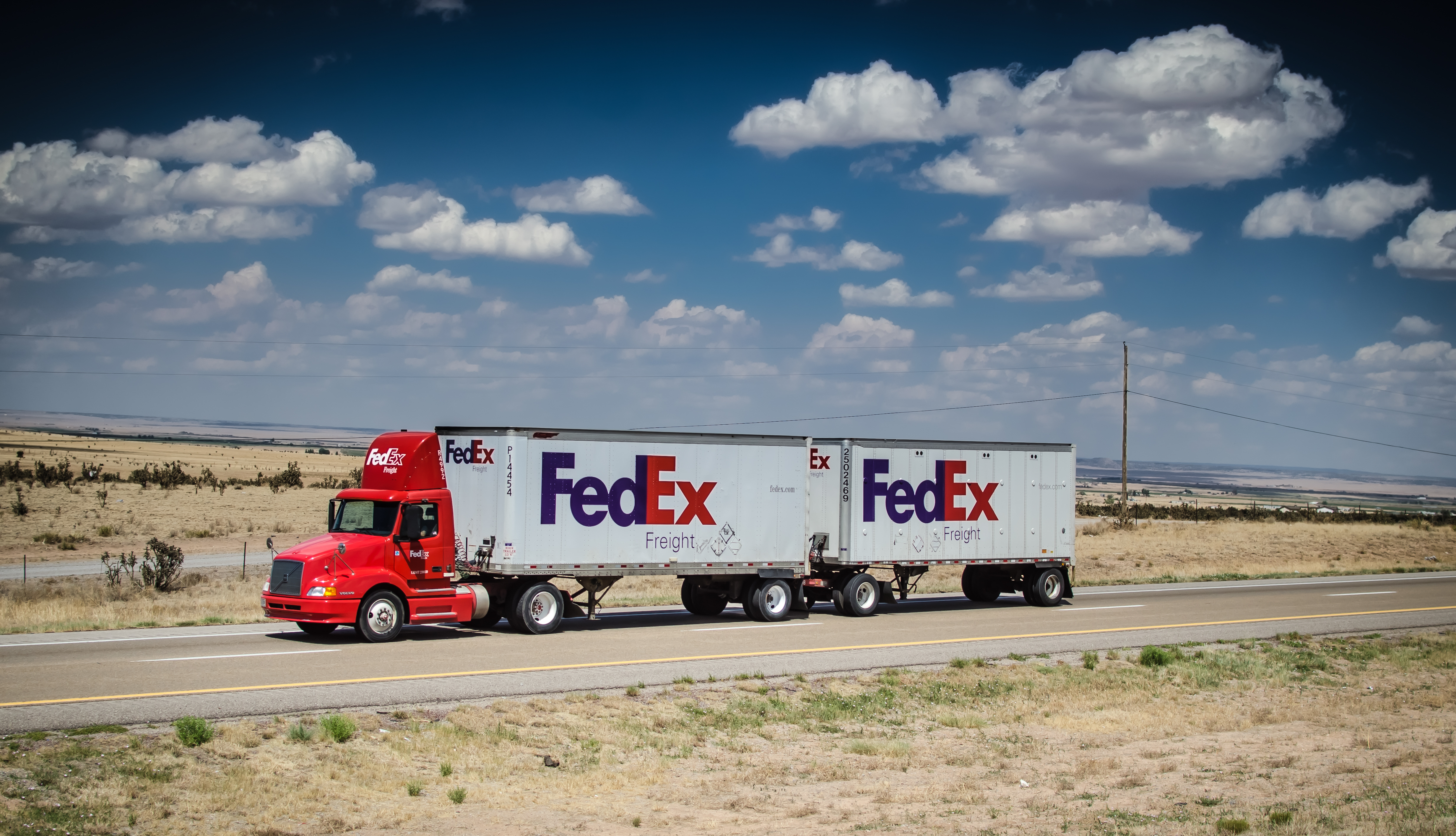 A FedEx truck with a double-trailer moves along a desert highway.