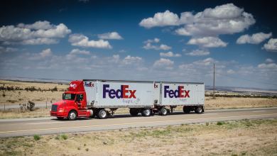 A FedEx truck with a double-trailer moves along a desert highway.