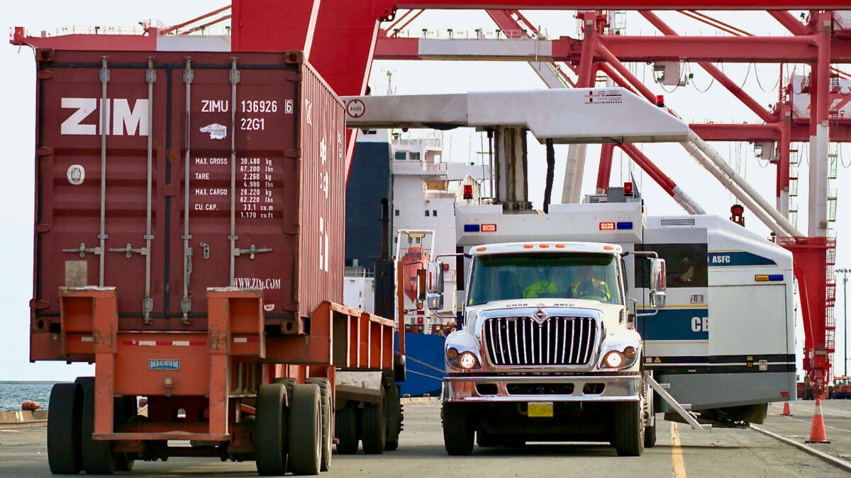 CBSA officers keep watch from a truck as an intermodal container prepares to roll by at a Canadian port.