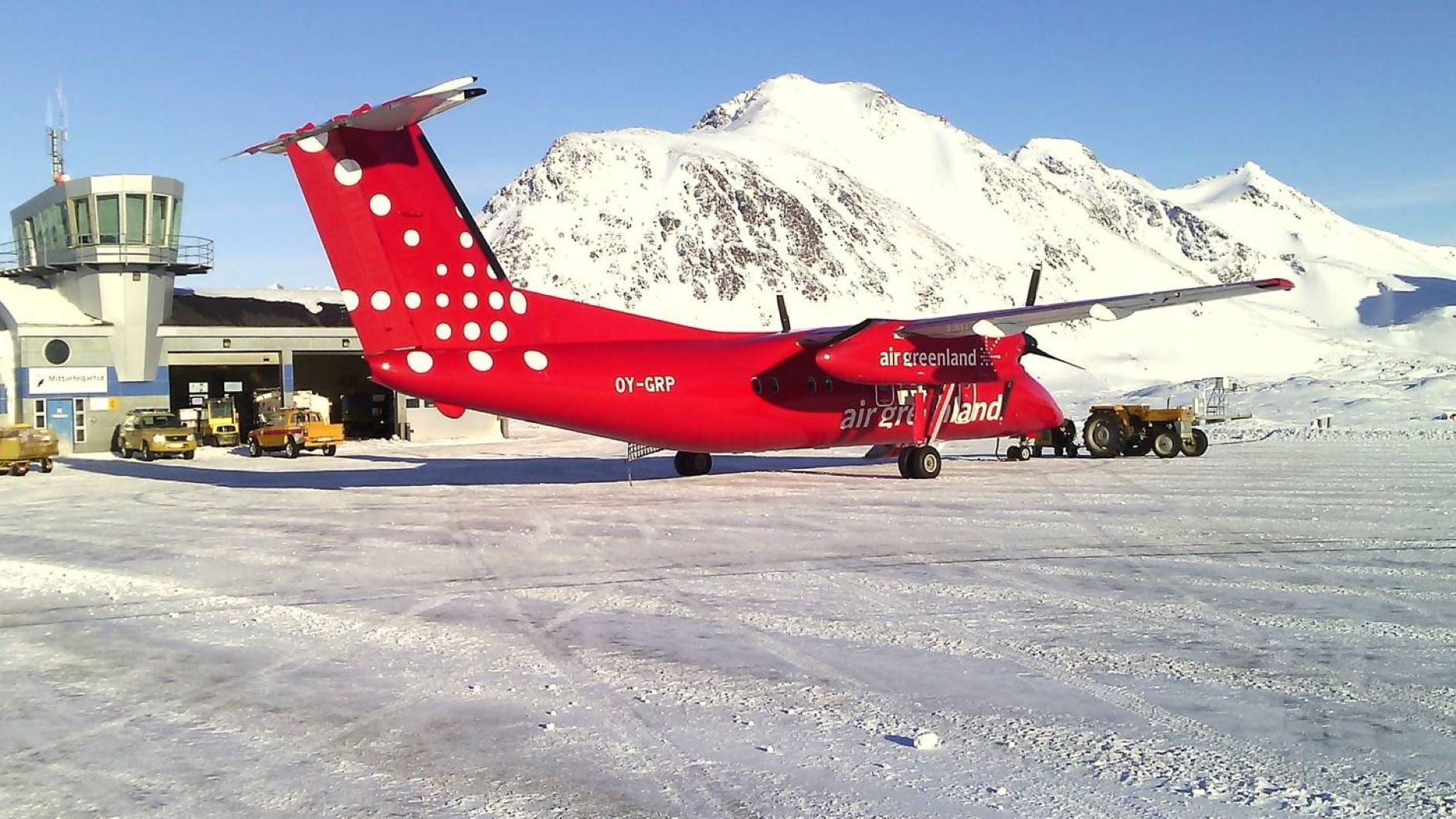 A turboprop plane on runway with snow-covered mountains in distance in Greenland.