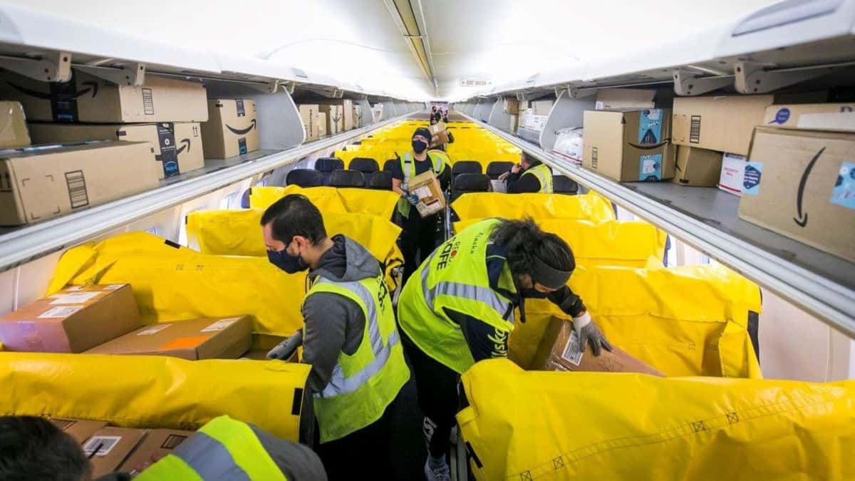 Workers put boxes in yellow seat bags in the passenger cabin of a plane.