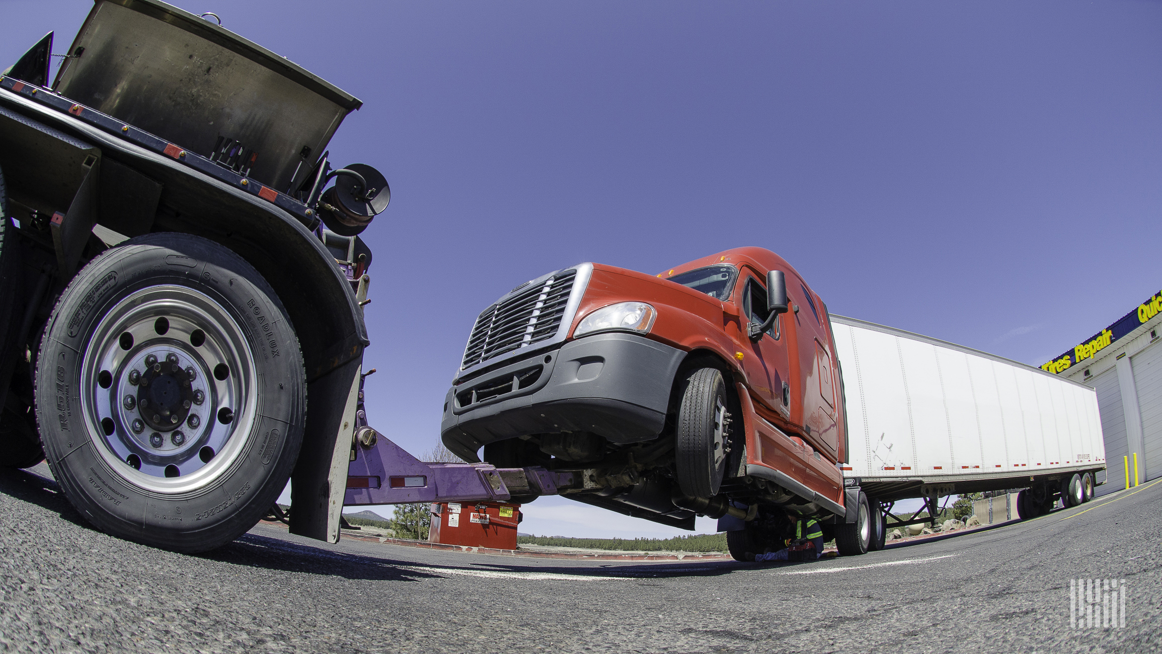 Tractor-trailer hitched to a tow truck at a repair shop.