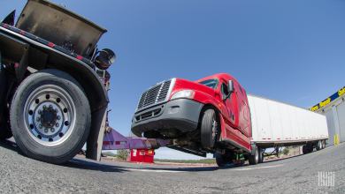 Tractor-trailer hitched to a tow truck at a repair shop.