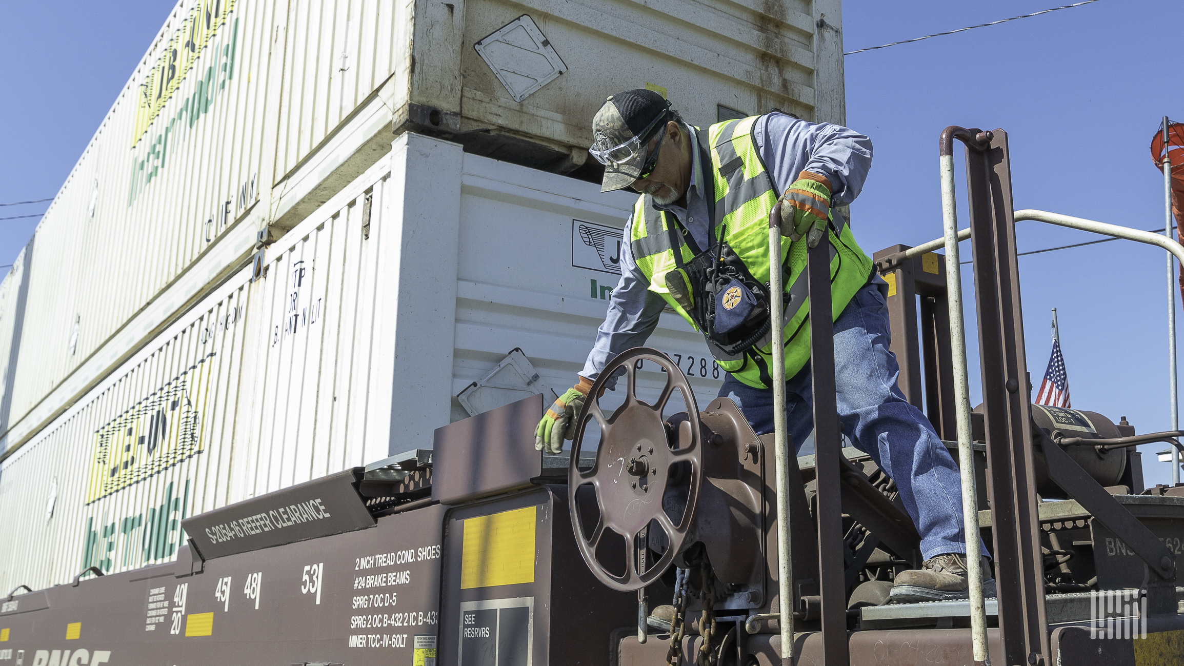 A photograph of a man turning the steel wheel of an intermodal car.