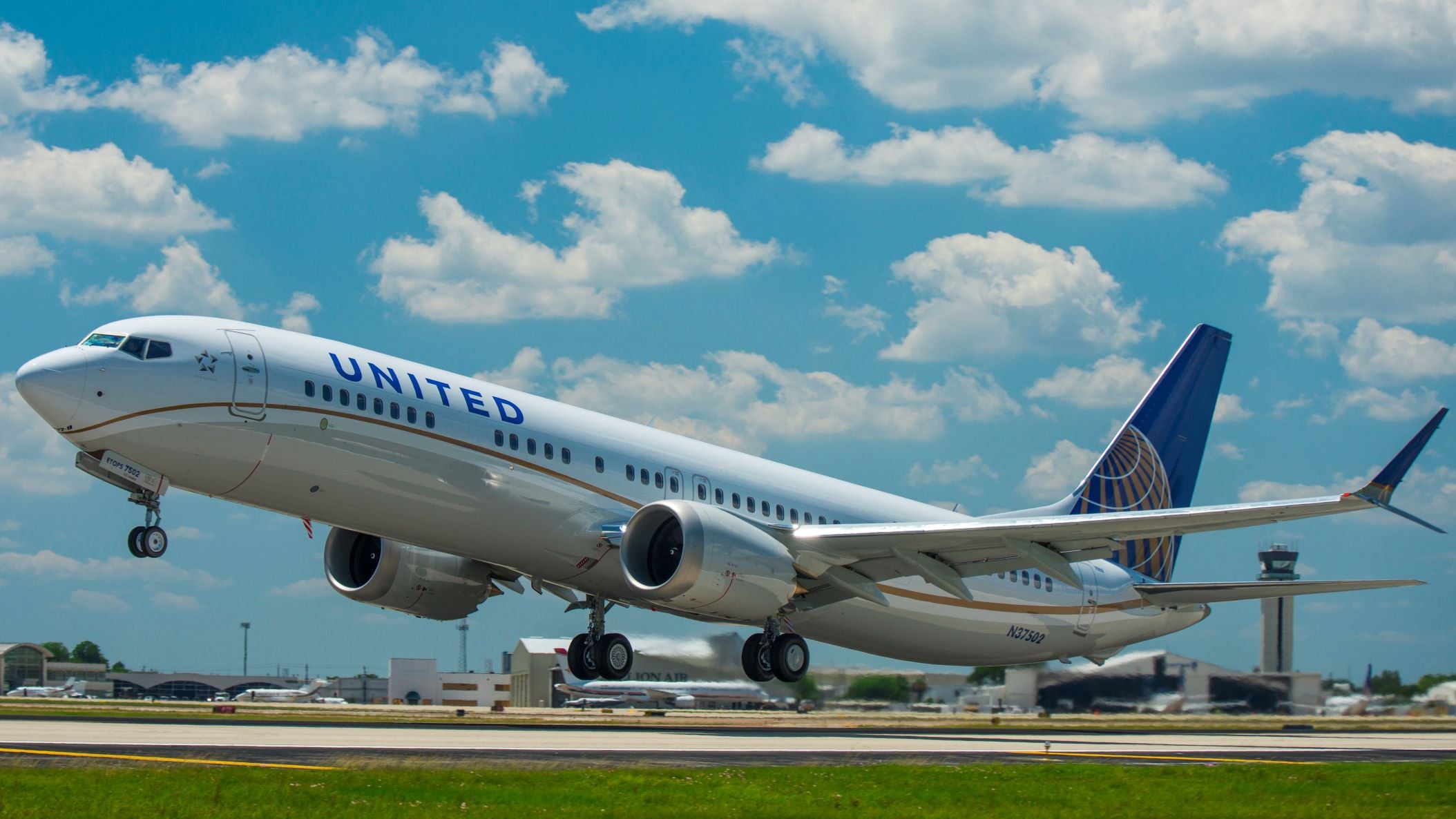 A United Airlines jet, with white fuselage and blue tail, lifts off from runway under bright blue sky with clouds.