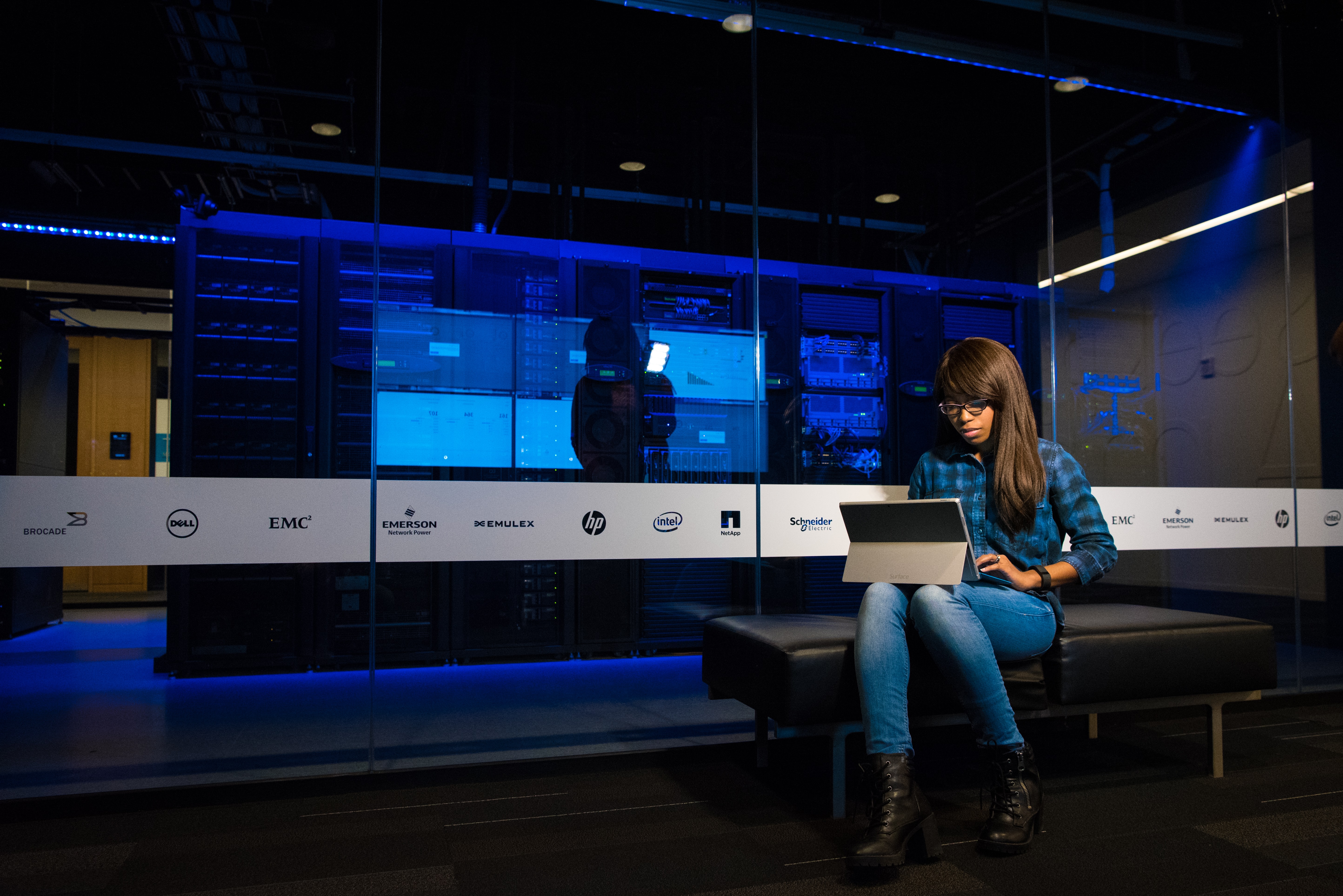 Woman using laptop in front of server stacks