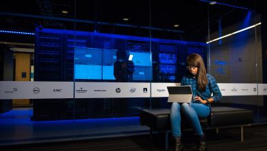 Woman using laptop in front of server stacks