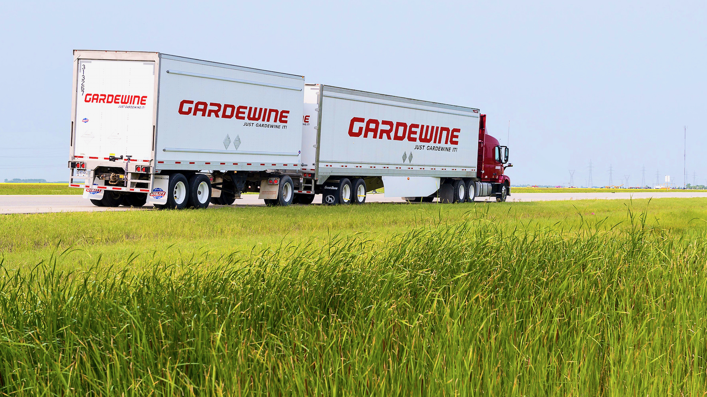 A red truck of Mullen Group carrier Gardewine pulling a double trailer, seen from the side.