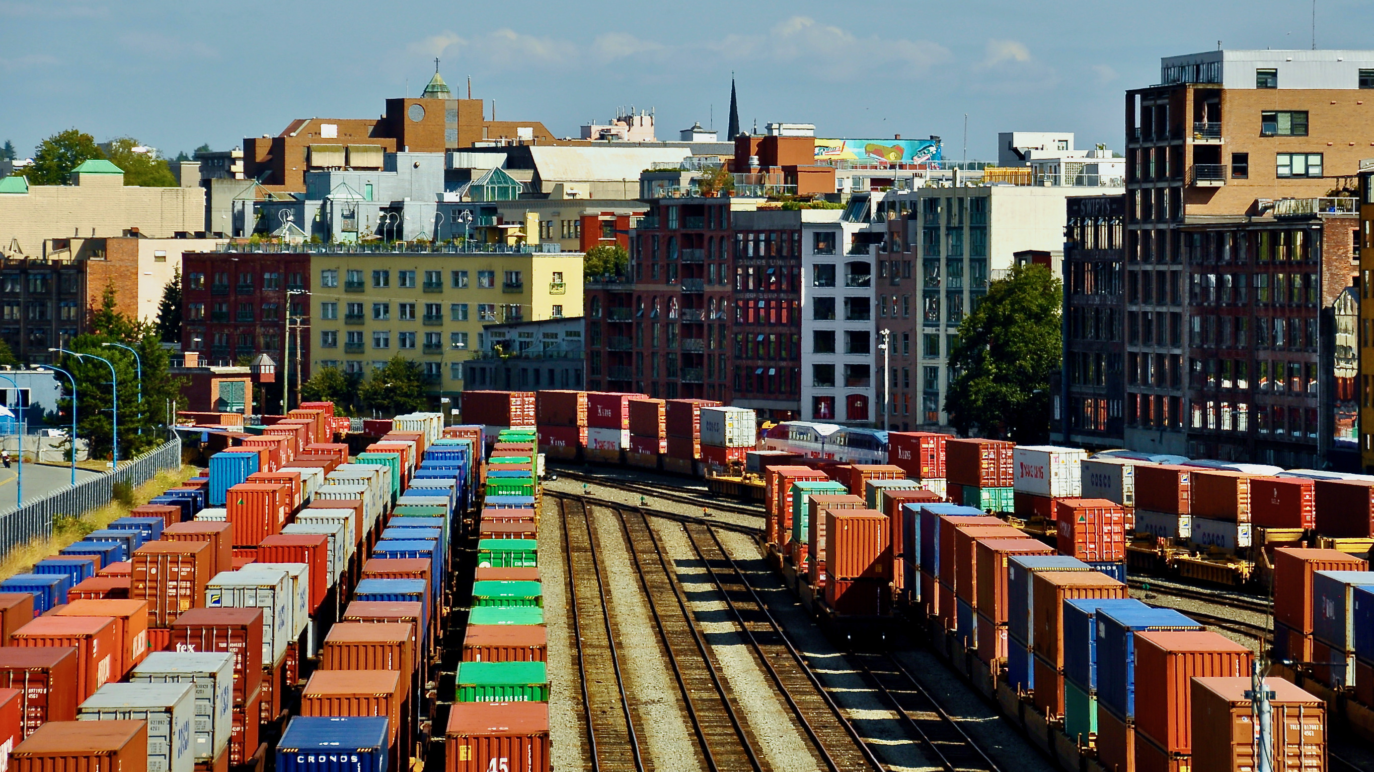 Rail cars loaded with intermodal containers near the port of Vancouver, with the city skyline behind it.