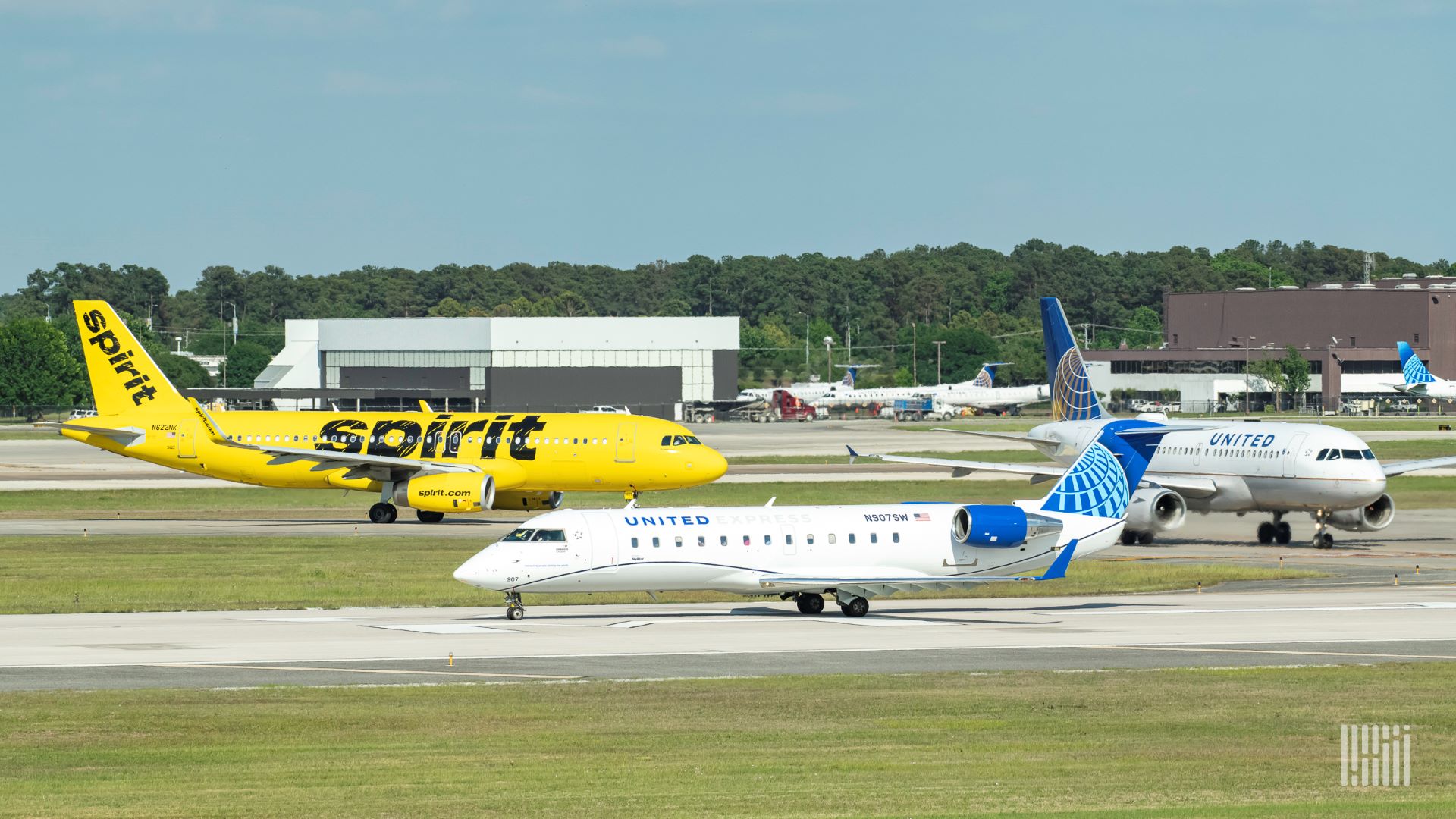 A yellow Spirit Airlines plane and two small United Airlines jets taxi around an airport.