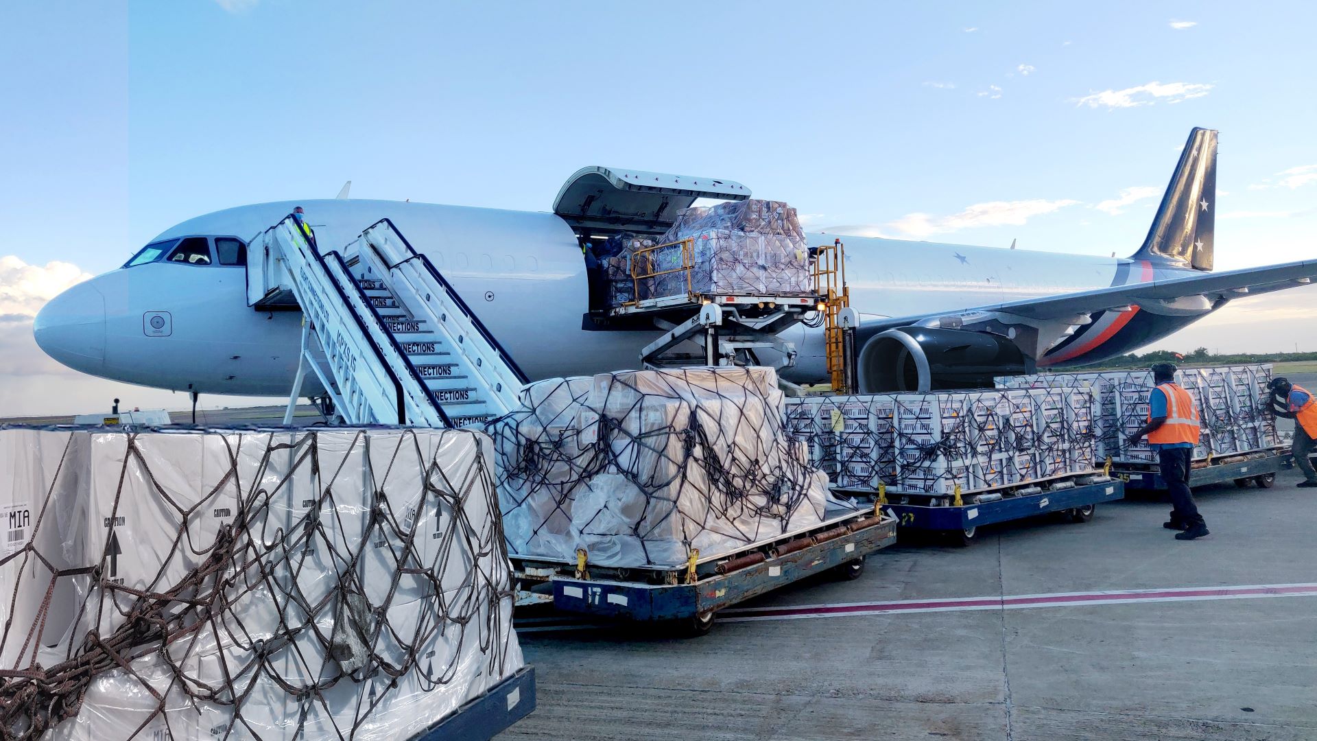 Ground-level view of cargo pallets on the tarmac being loaded on a white aircaft.