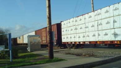 A photograph of a train rolling past a rail crossing.
