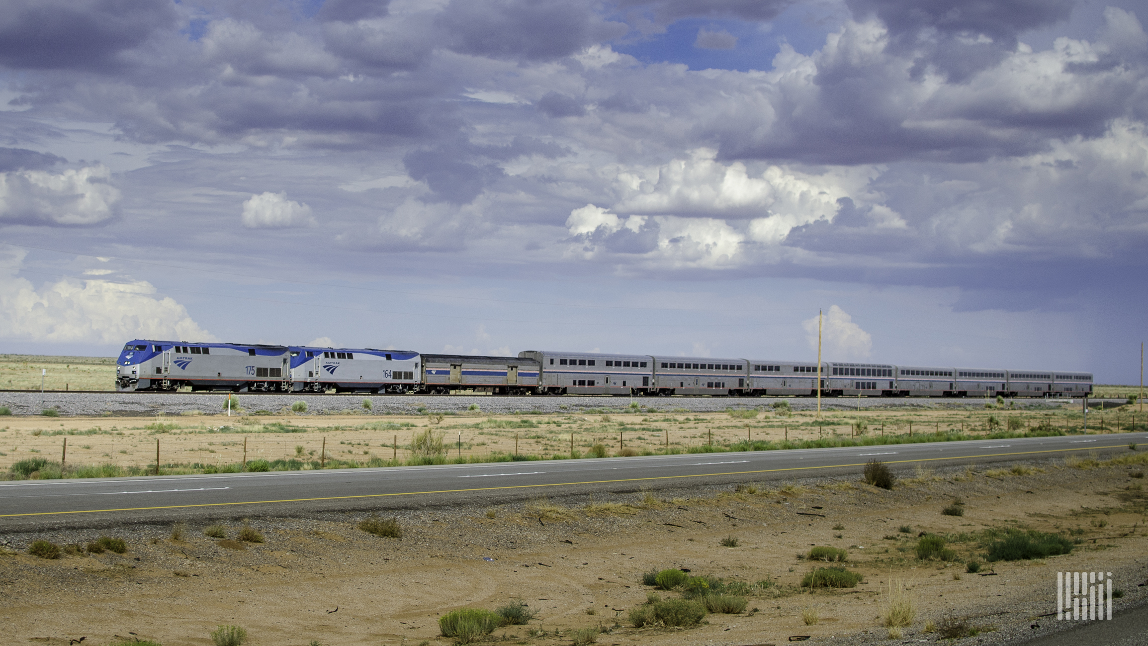 A photo of an Amtrak train travelling through a flat and grassy plain.