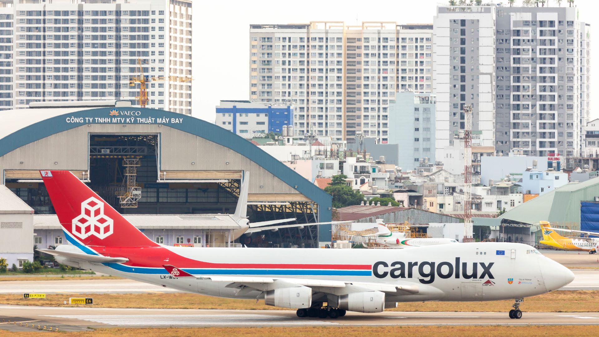 A Cargolux jumbo jet taxing at airport with Ho Chi Minh City apartments in background.