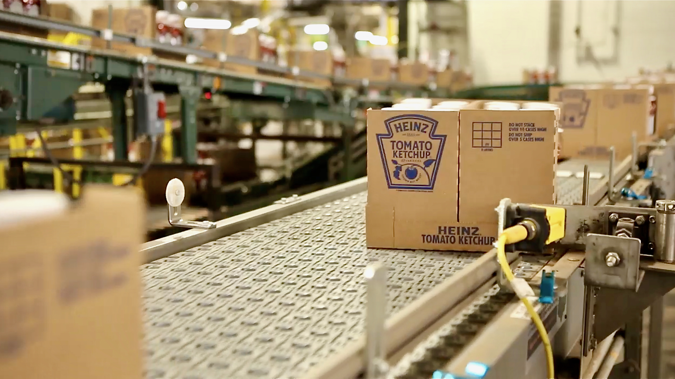 A cardboard box of Heinz ketchup moves on a conveyer belt, illustrating an article about Kraft Heinz.