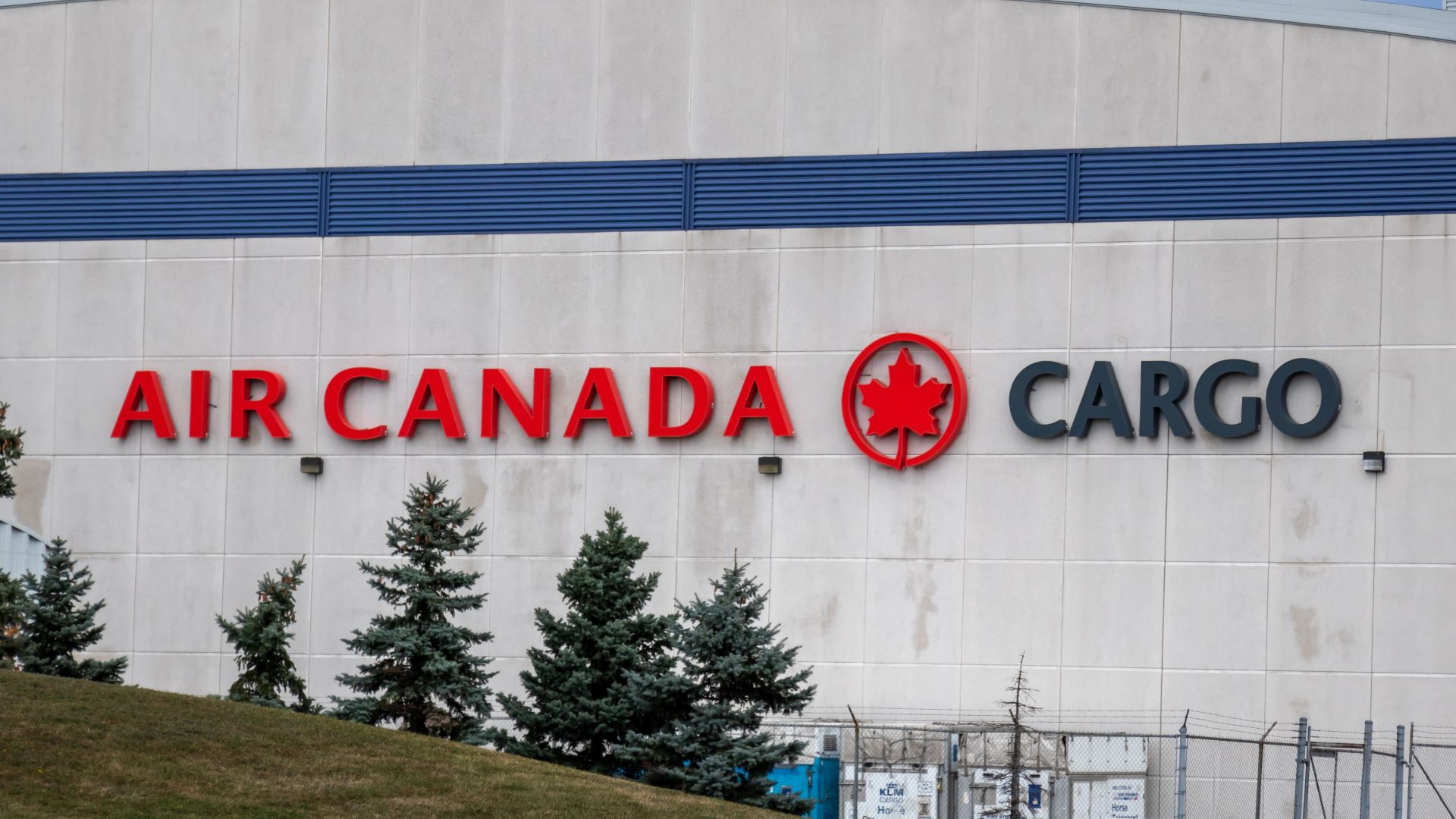 Air Canada Cargo lettering on side of building with some pine trees in foreground.