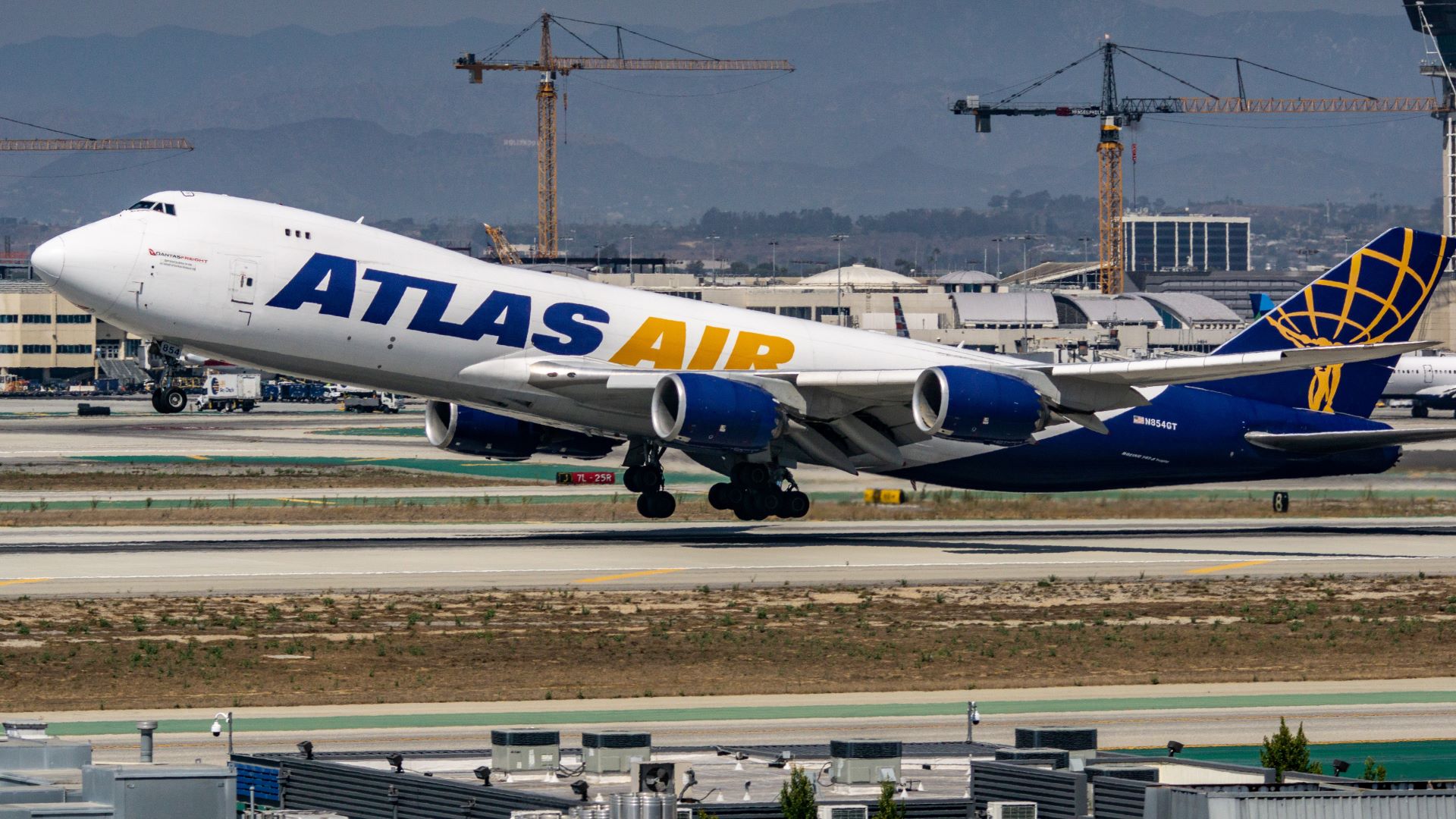 An Atlas Air jumbo cargo jet takes off, with front wheel in air. The plane is white, with purple and gold lettering.