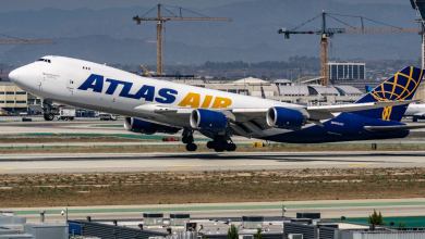 An Atlas Air jumbo cargo jet takes off, with front wheel in air. The plane is white, with purple and gold lettering.