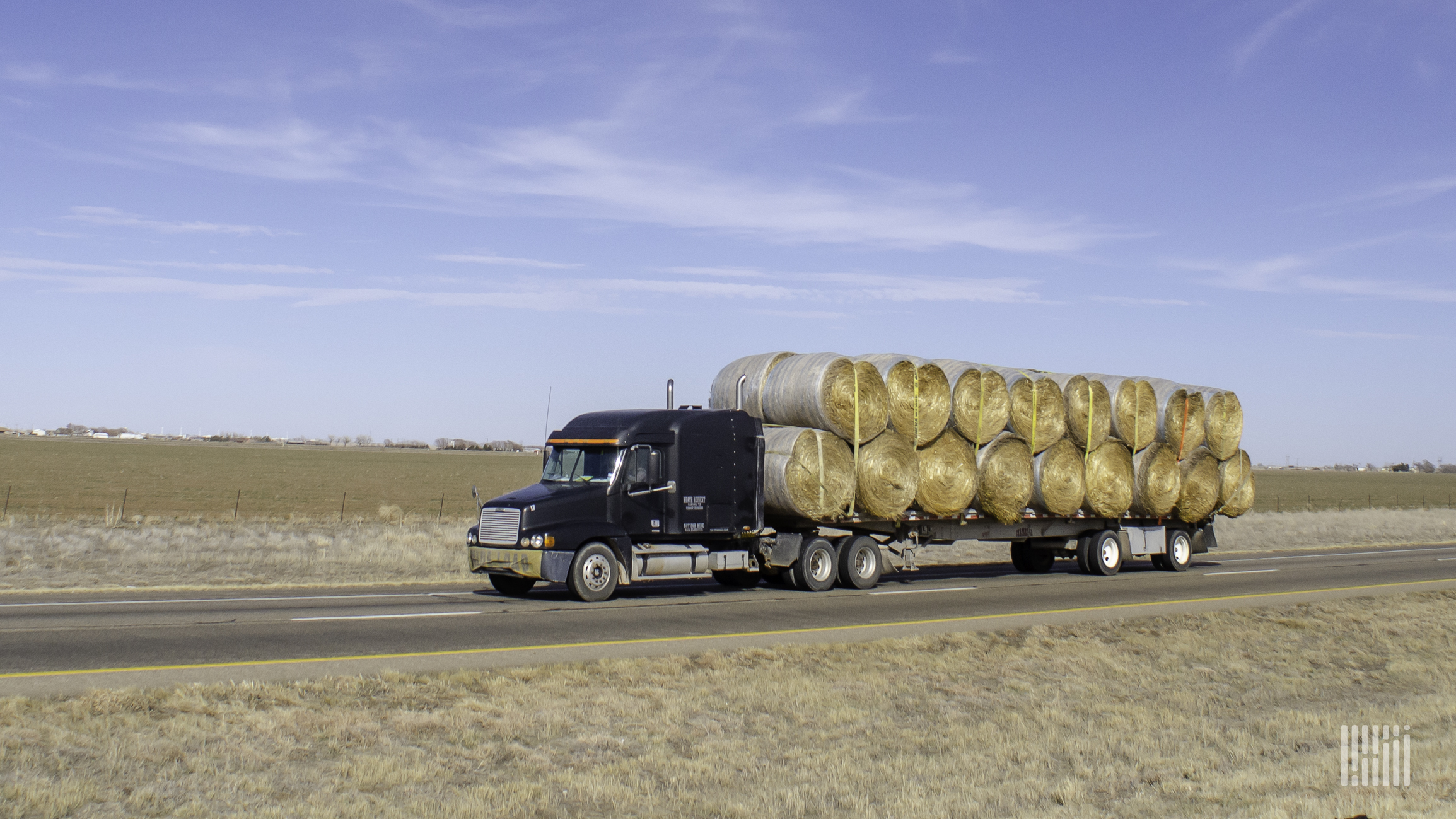 Flatbed truck carrying large bales of hay.