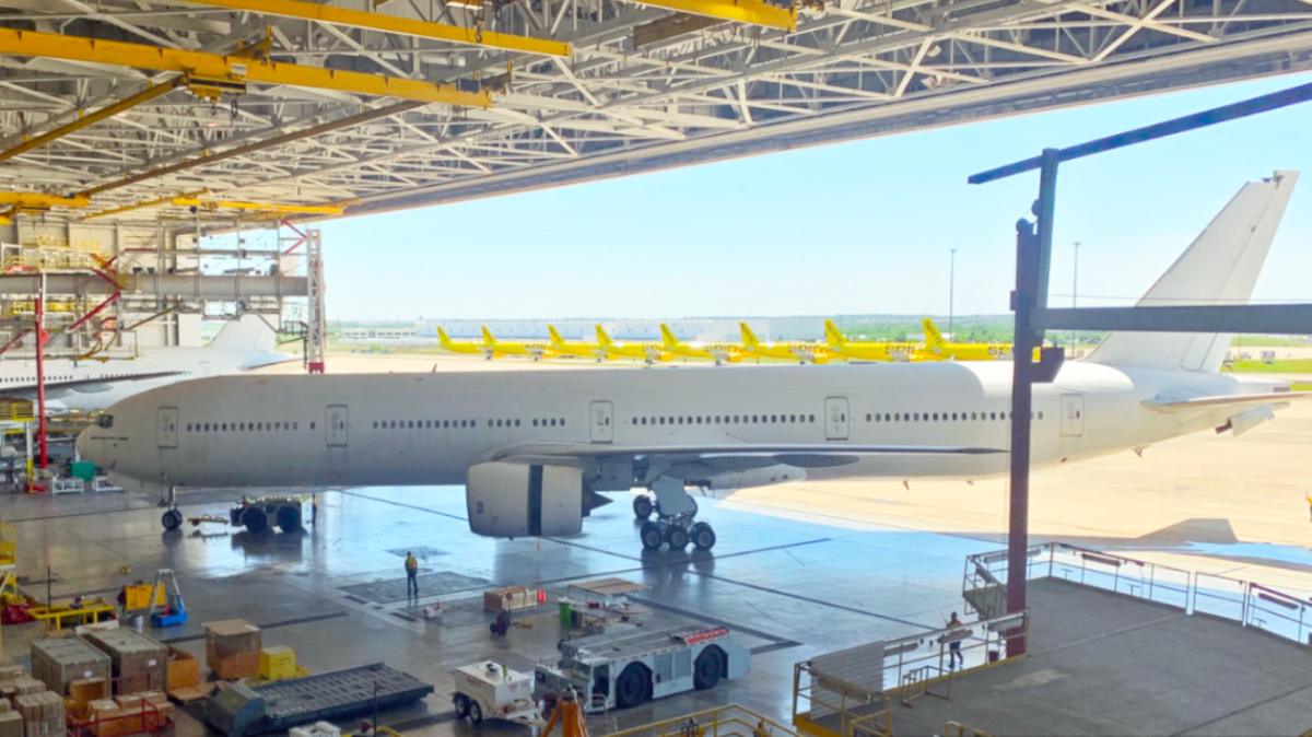 A large white jet is moved through the door of a large airplane hangar.