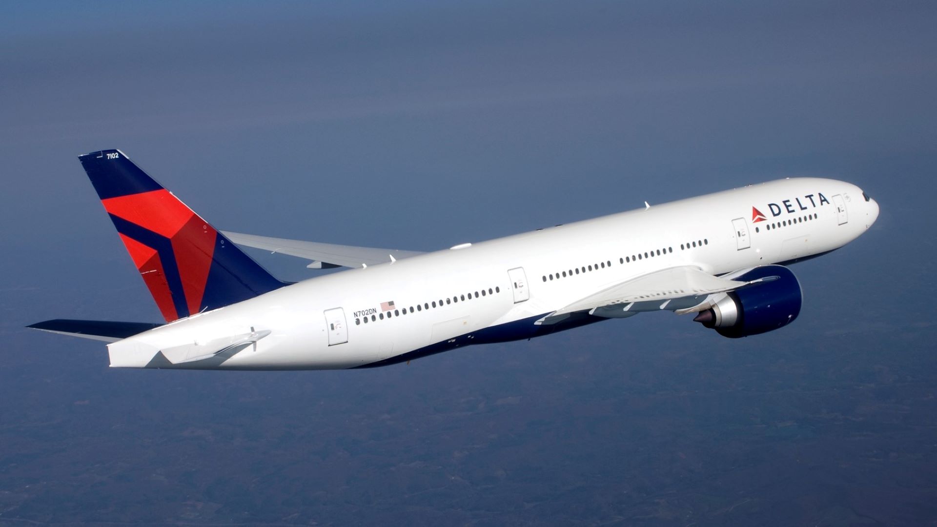 A Delta Air Lines jet with white body and blue/red tail in flight, as viewed from side rear.