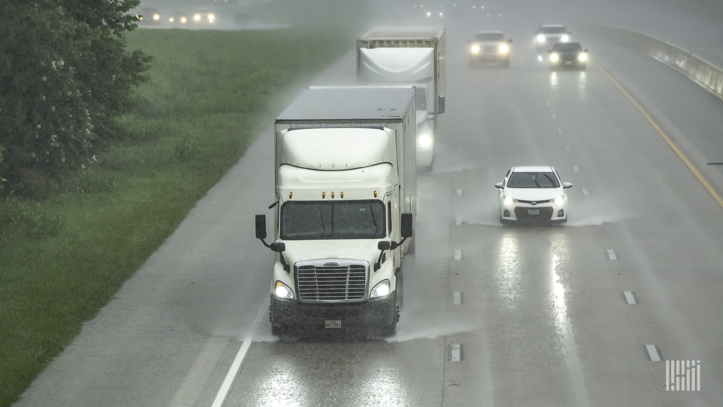 Tractor-trailers on a highway in heavy rain.