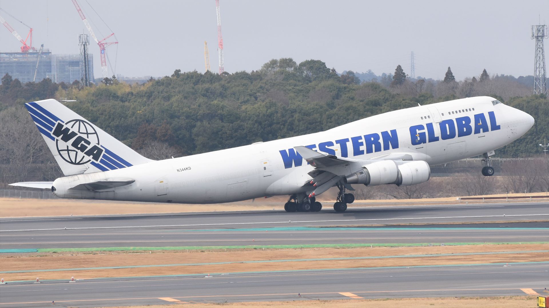 A white jumbo jet with blue lettering takes off with nose lifted in air.