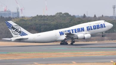 A white jumbo jet with blue lettering takes off with nose lifted in air.