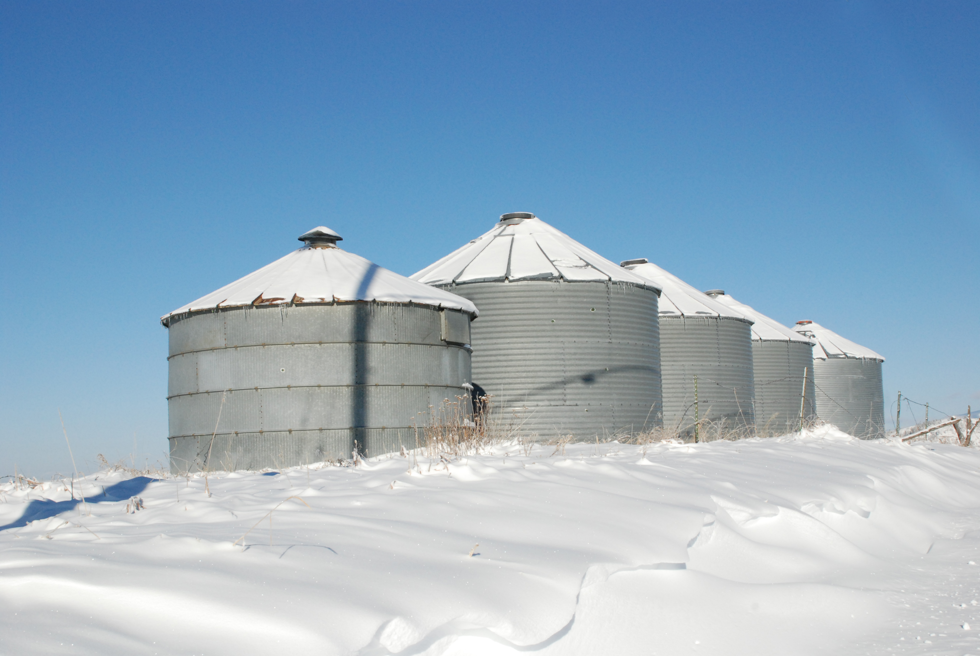 A photograh of grain bins in a snowy field.