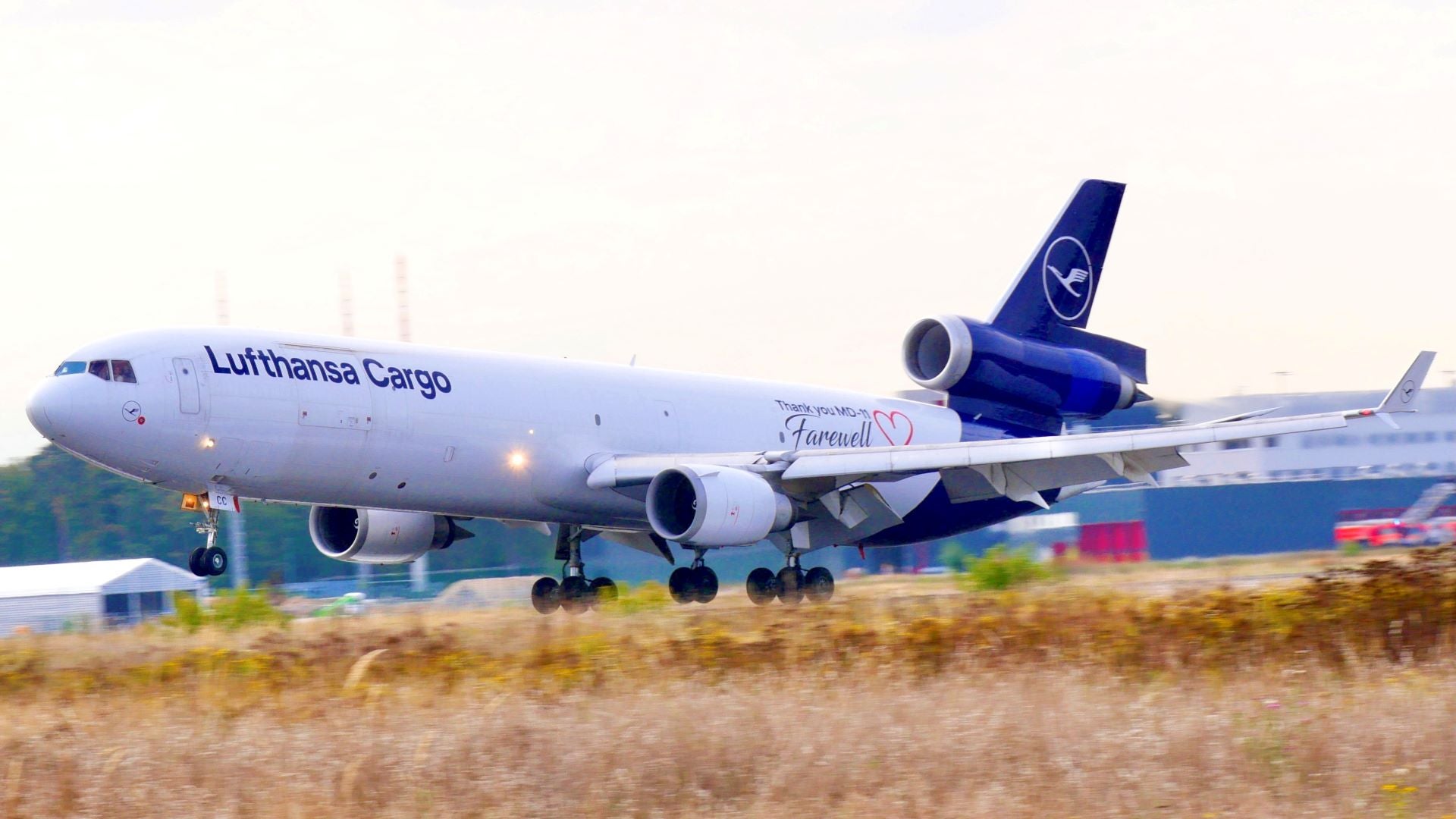 A white Lufthansa plane with a blue tail touches down on runway with grass in median.