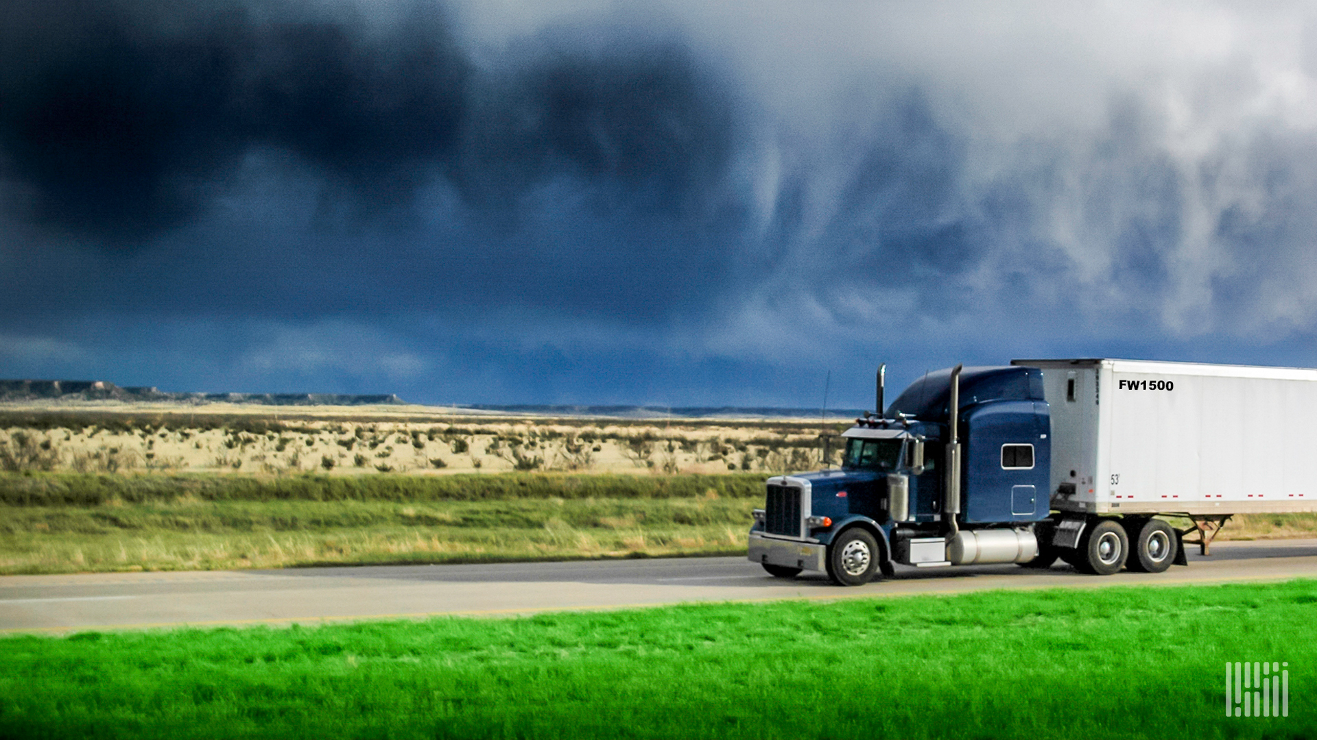 Tractor-trailer on a highway with dark storm cloud across the sky.