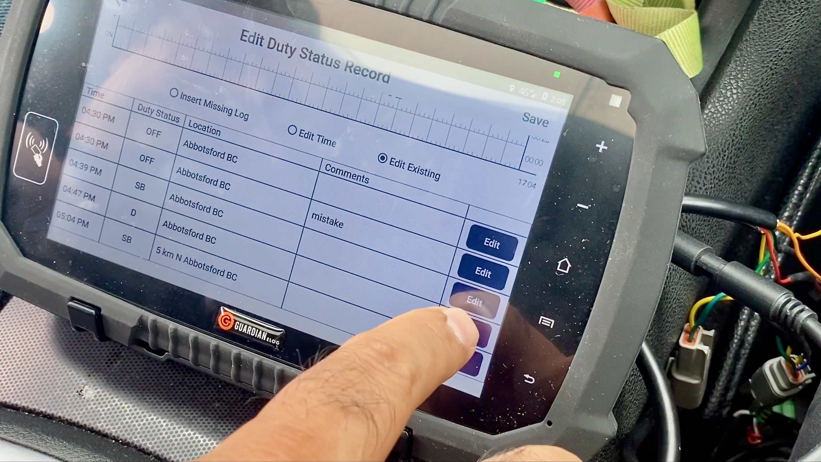 An electronic logging device screen being edited, with a finger being shown pushing a button on the screen.