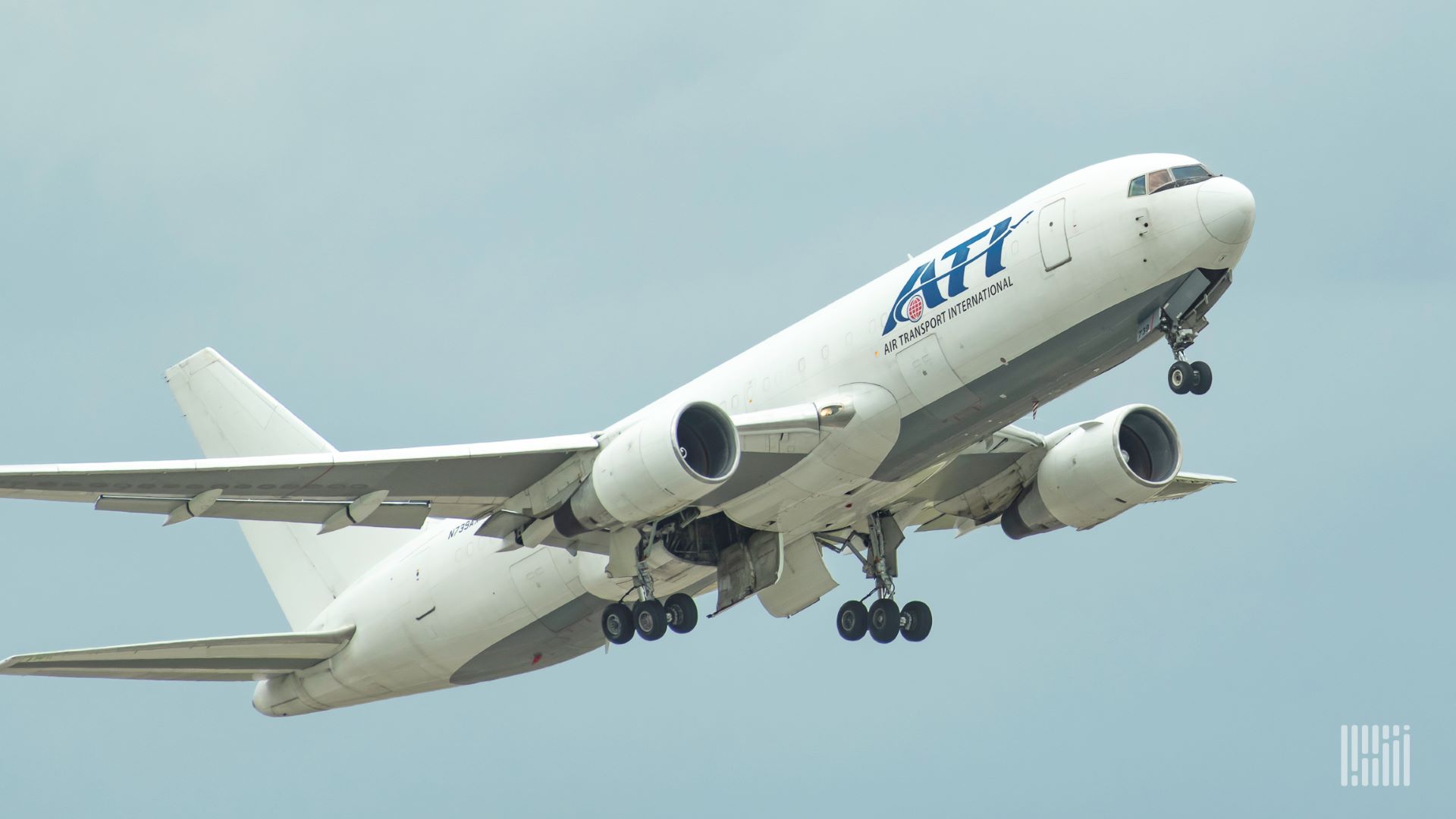 A white cargo jet with wheels down takes off against a gray sky.