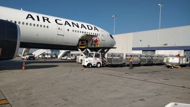 White Air Canada jet with cargo containers on the ground ready to load. Photo from side looking to forward half of the plane.
