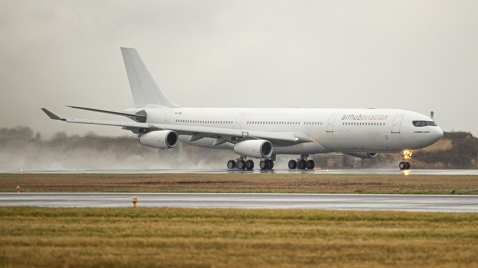 A large white plane with Airhub Airlines brand touches down on runway on gray day.