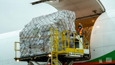 A large cargo container on a hydraulic lift being loaded into the side door of a cargo plane.