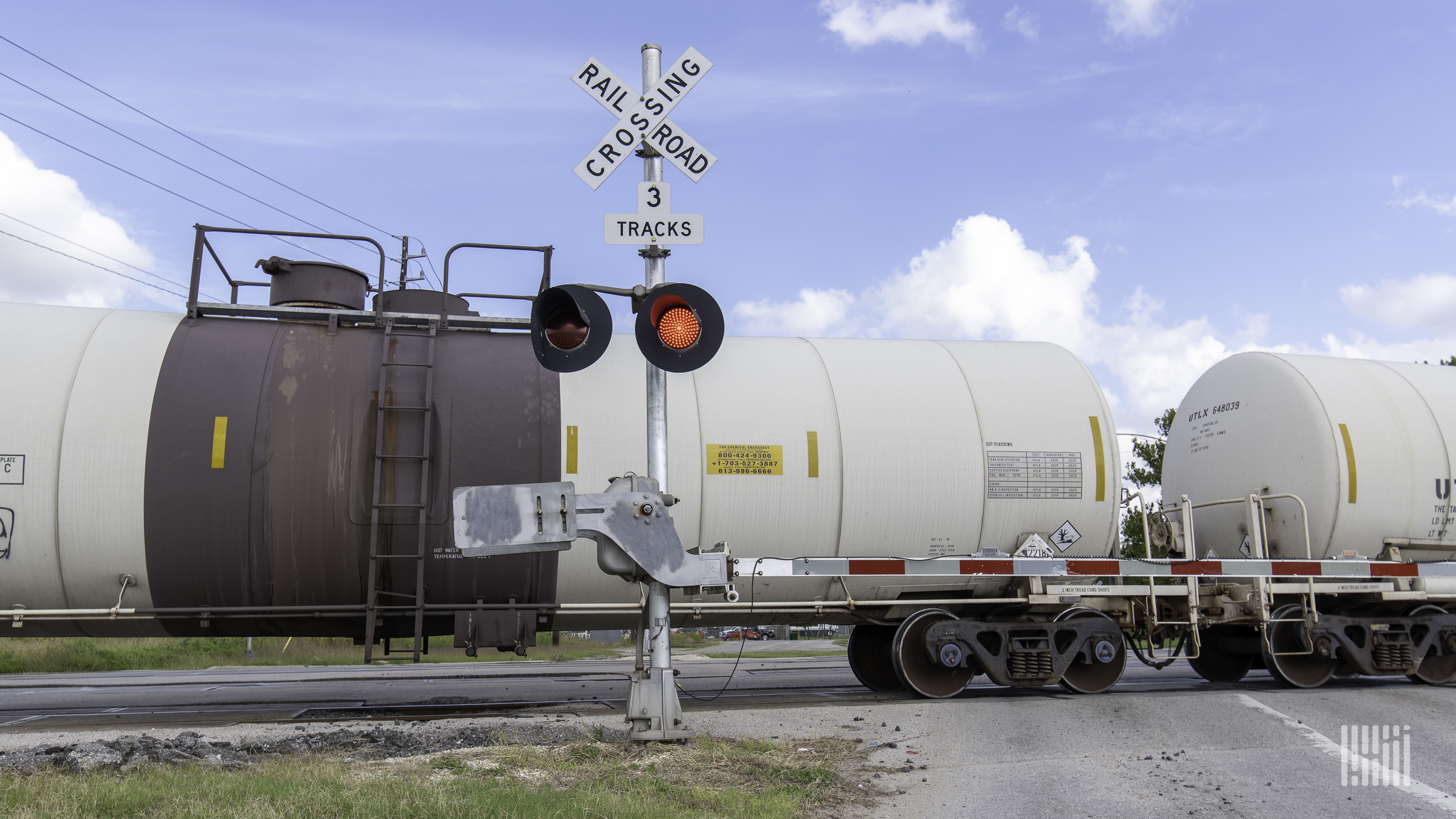 A photograph of a freight train rolling by a rail crossing.