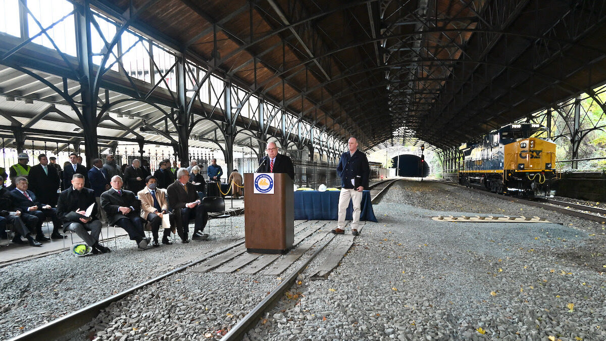 A photograph of rail tracks underneath a bridge. A group is sitting to the left under the bridge.