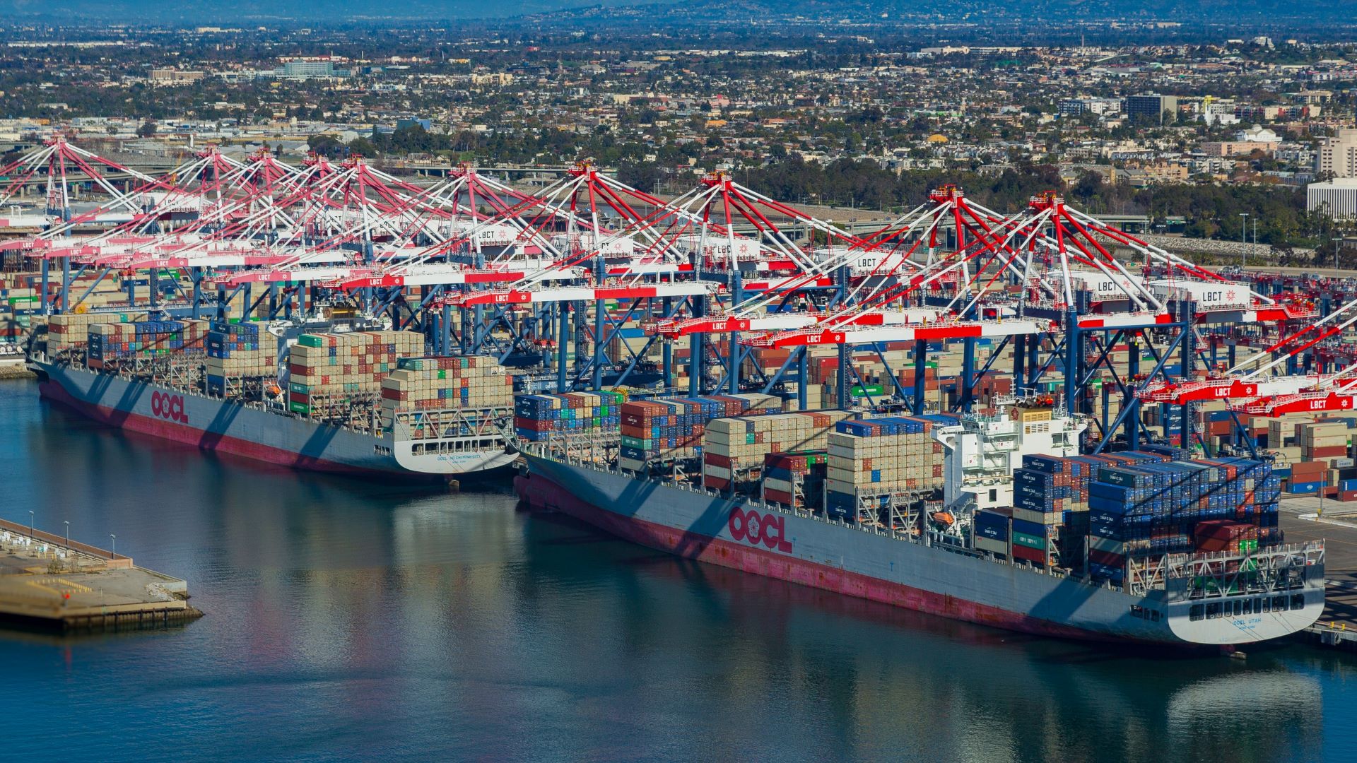 Two large container ships at a port, with cranes and containers on the docks.