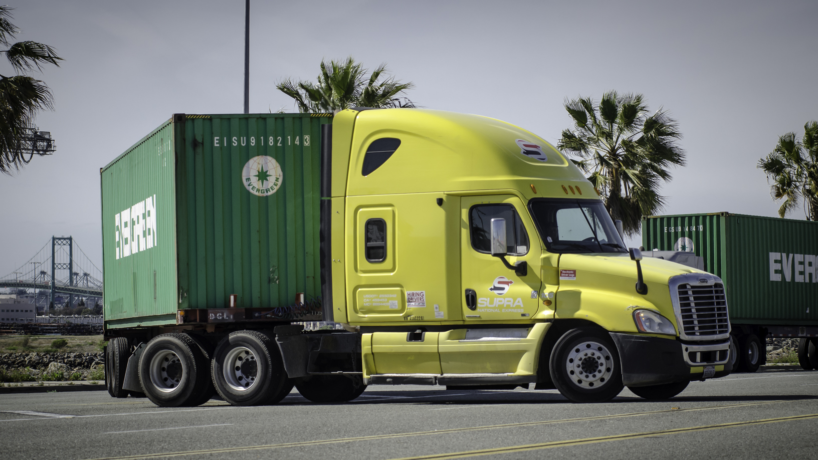 A yellow truck tractor with green trailer makes a turn.