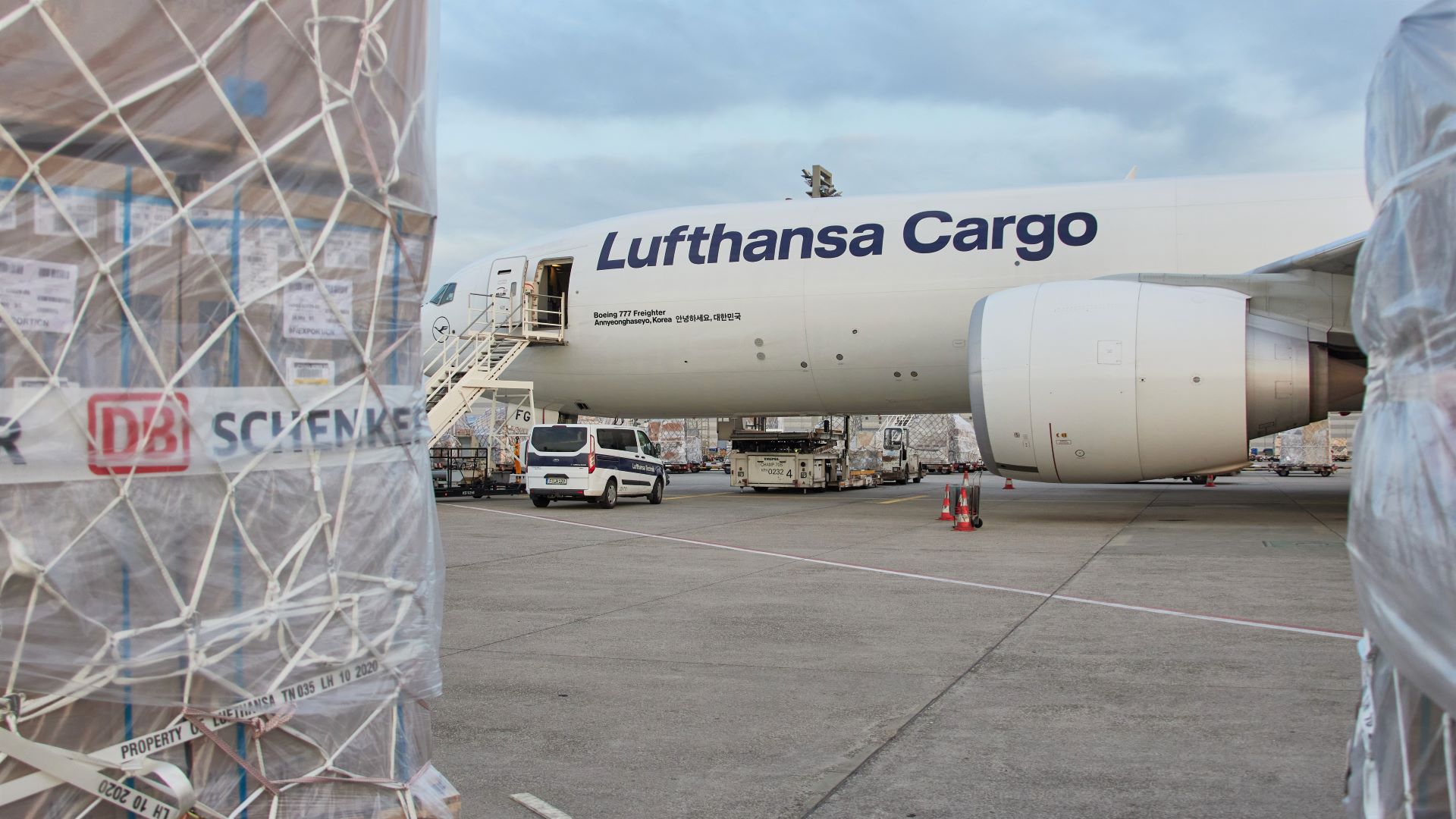 A plastic-wrapped cargo pallet in foreground, with a Lufthansa Cargo jet in the background.