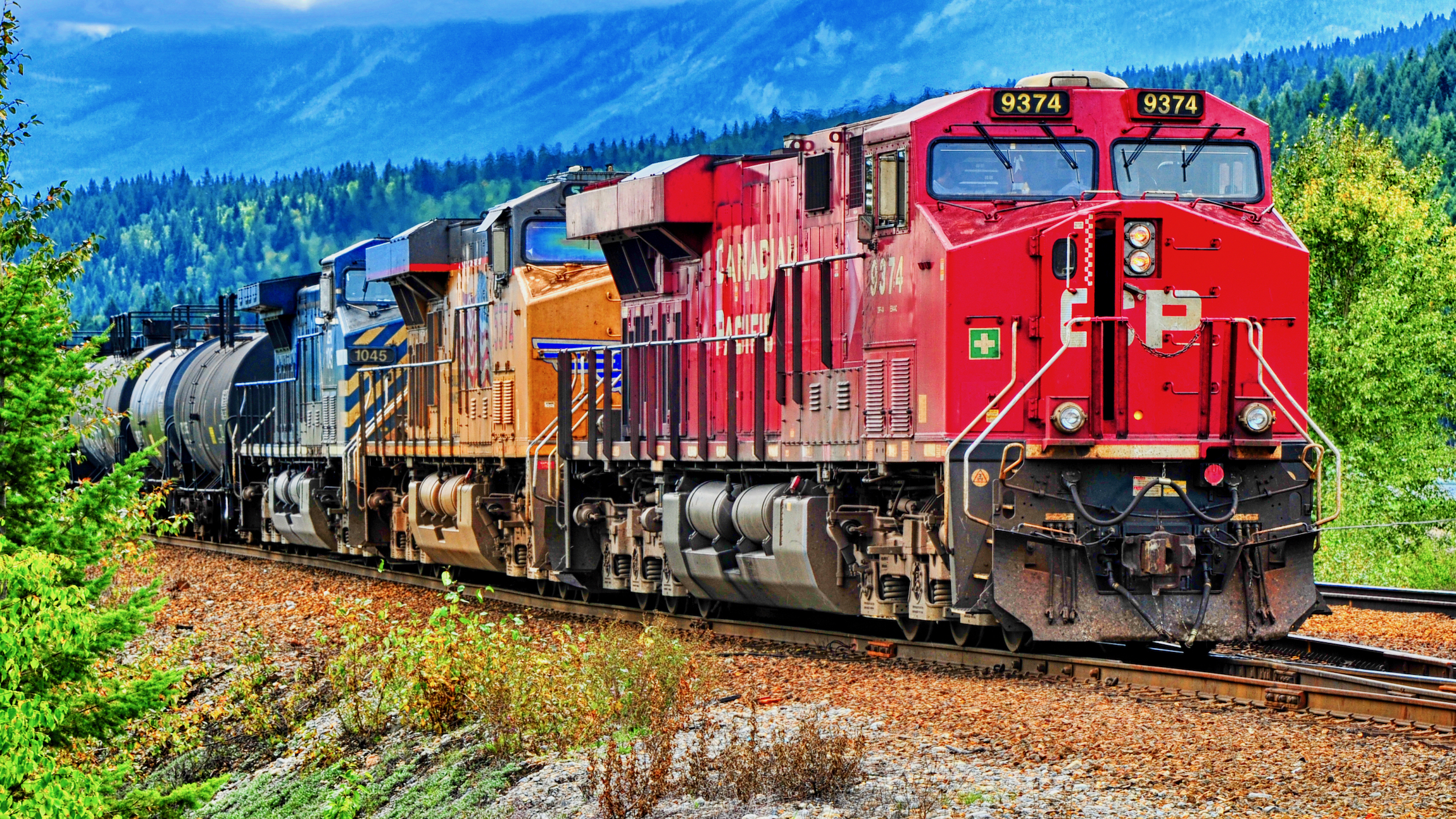 A Canadian Pacific or PC train engine moves on a train track with rail cars behind it.