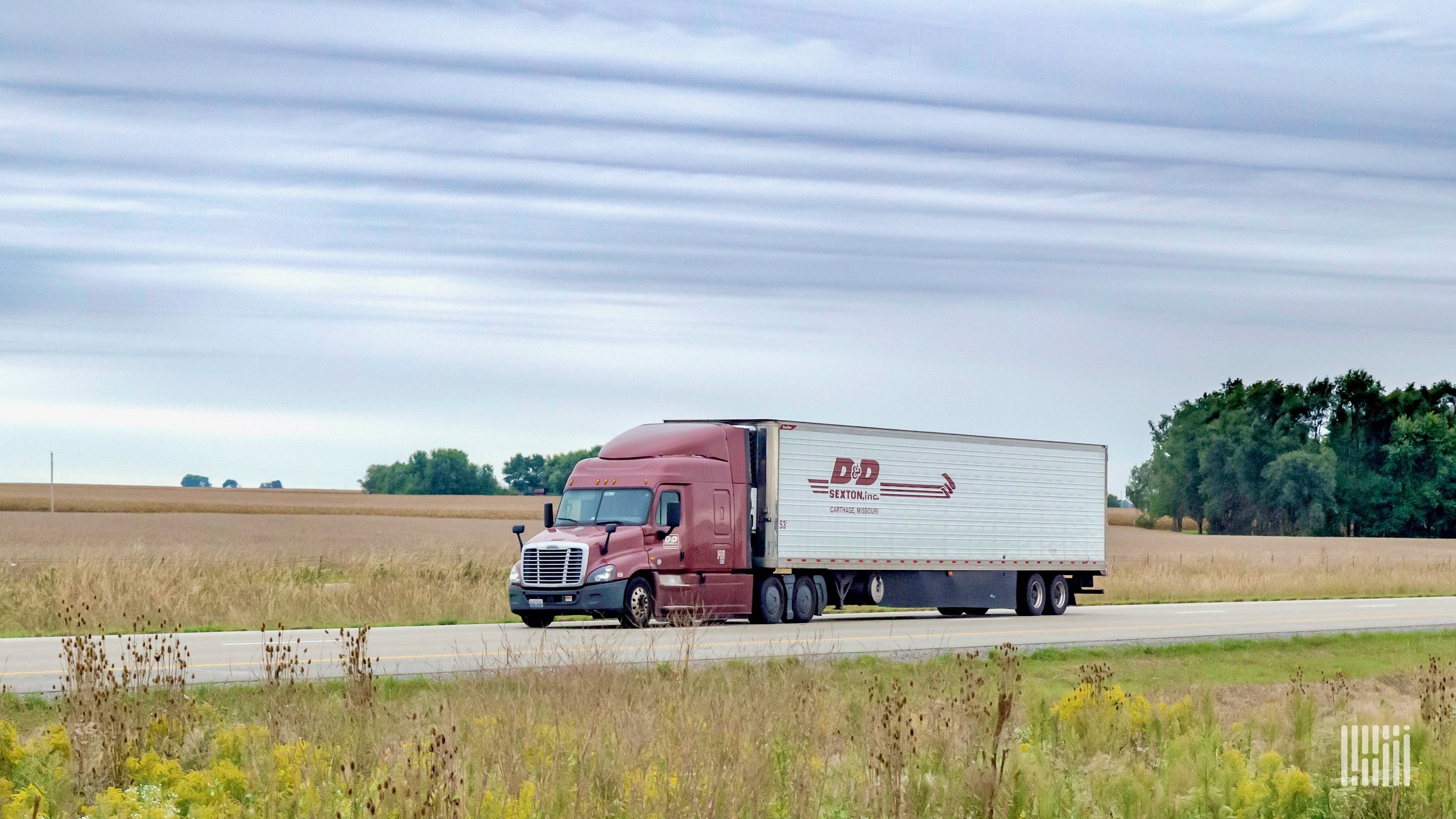 A tractor-trailer of D&D Sexton, which was acquired by TFI International, travels on a highway with fields in background.