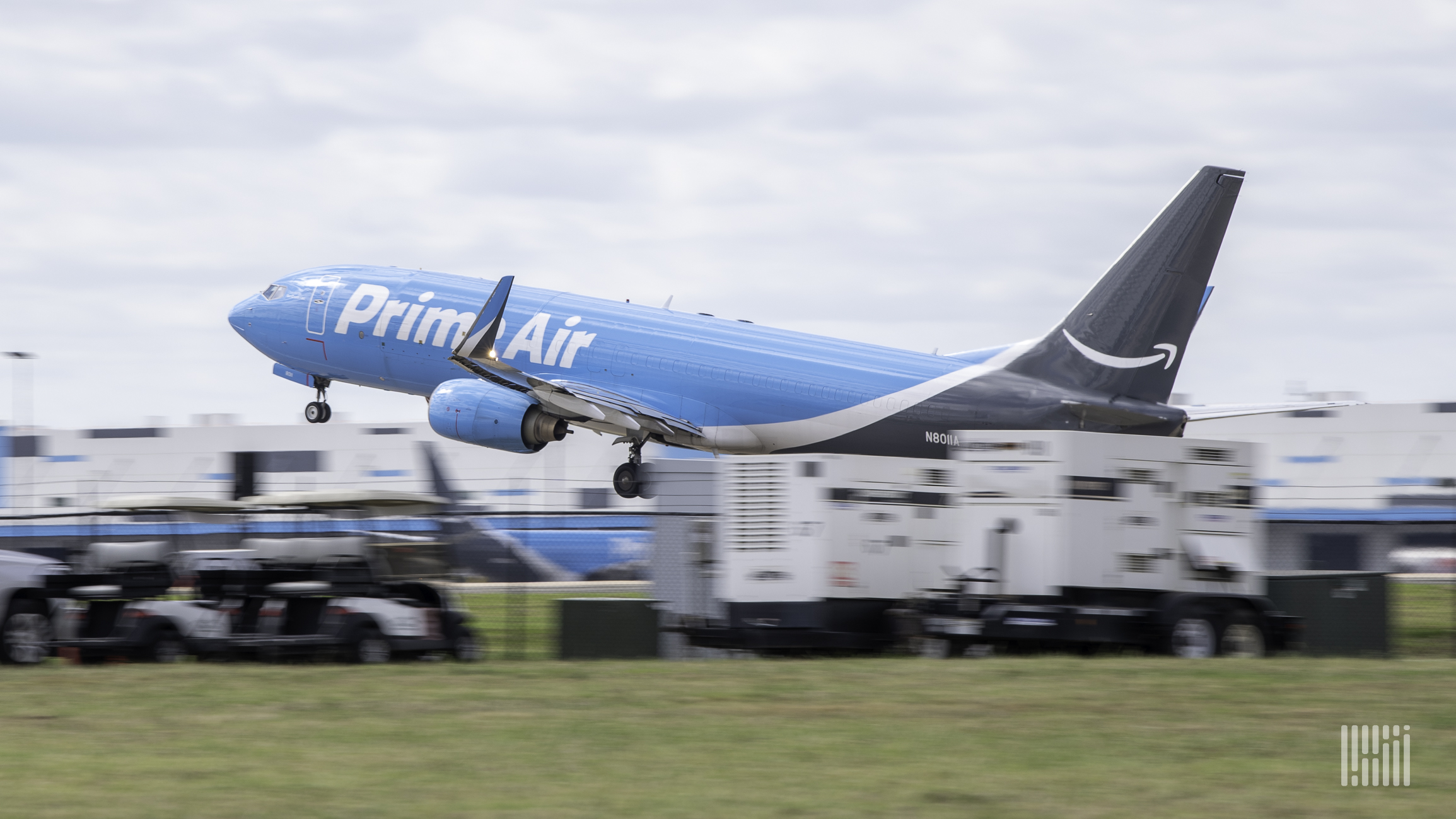 A light blue Amazon Air plane takes off, view from side rear.