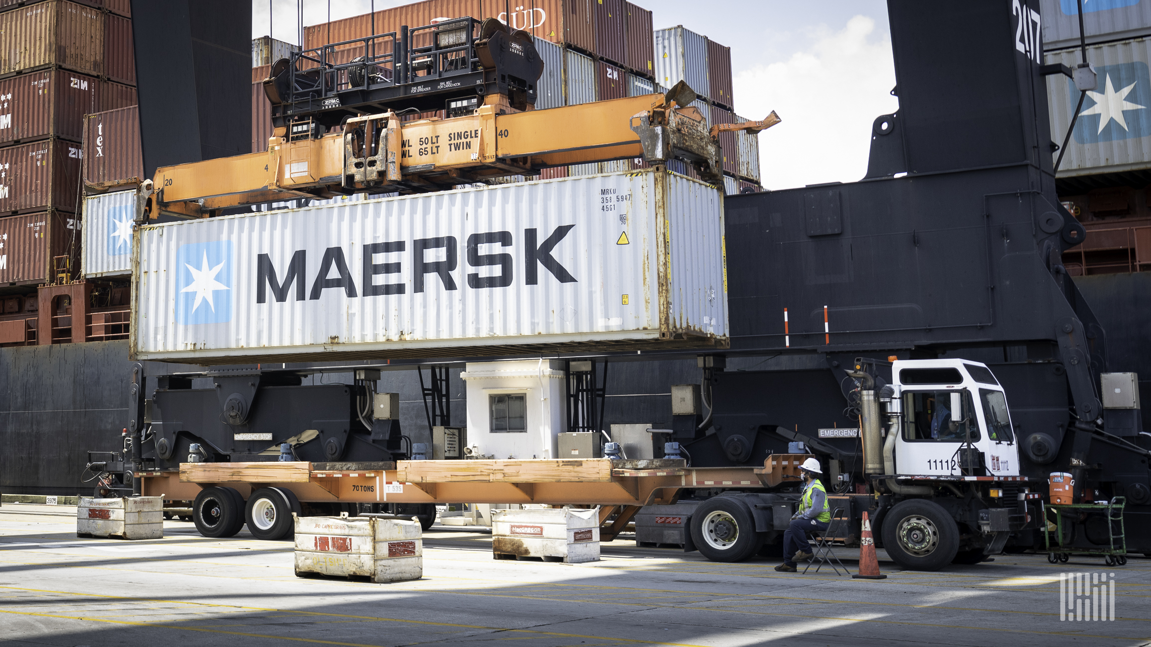 A Maersk shipping container is lowered on dock by a crane.