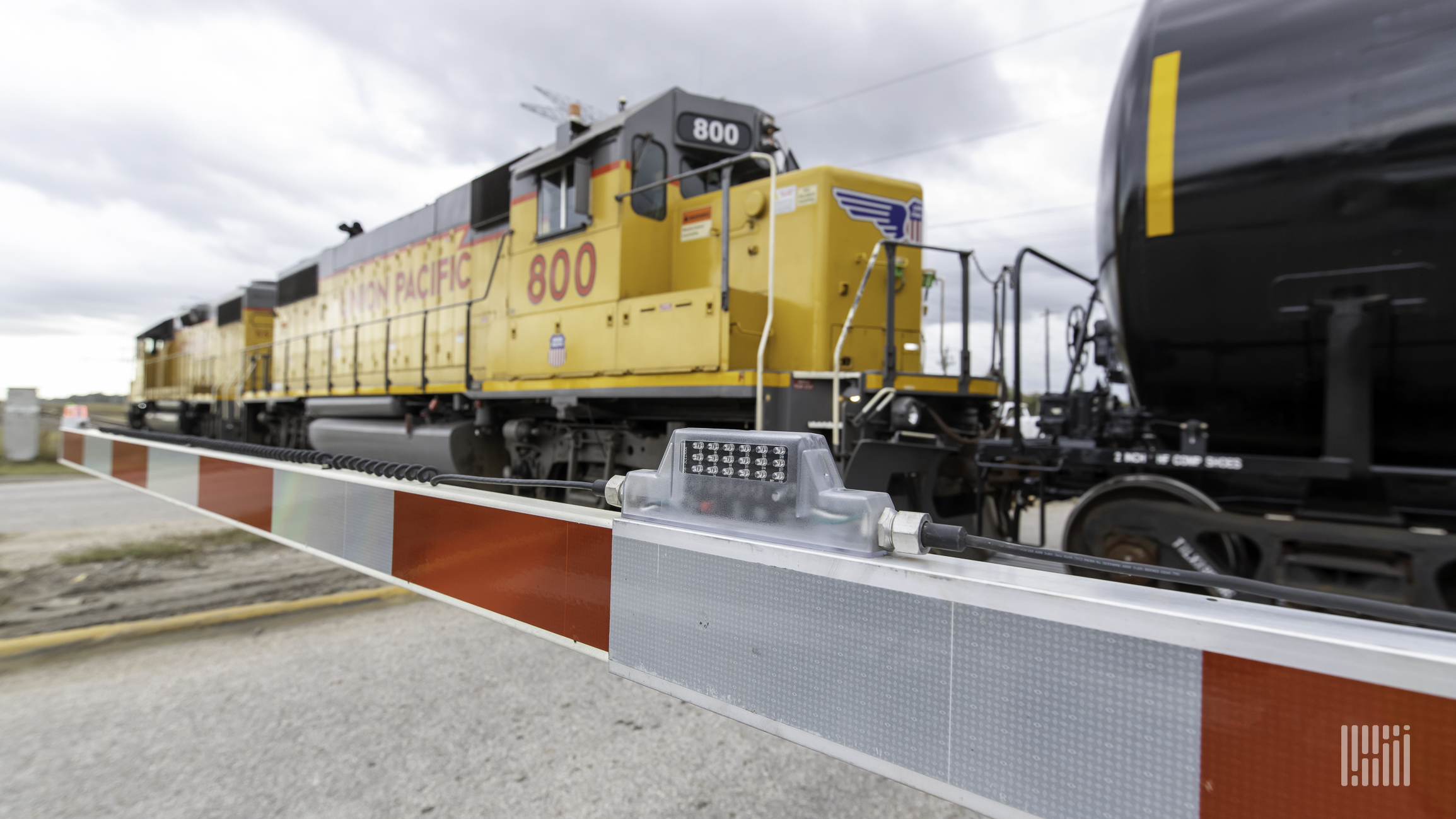 A photograph of a Union Pacific locomotive and a tank car rolling by a railroad crossing.