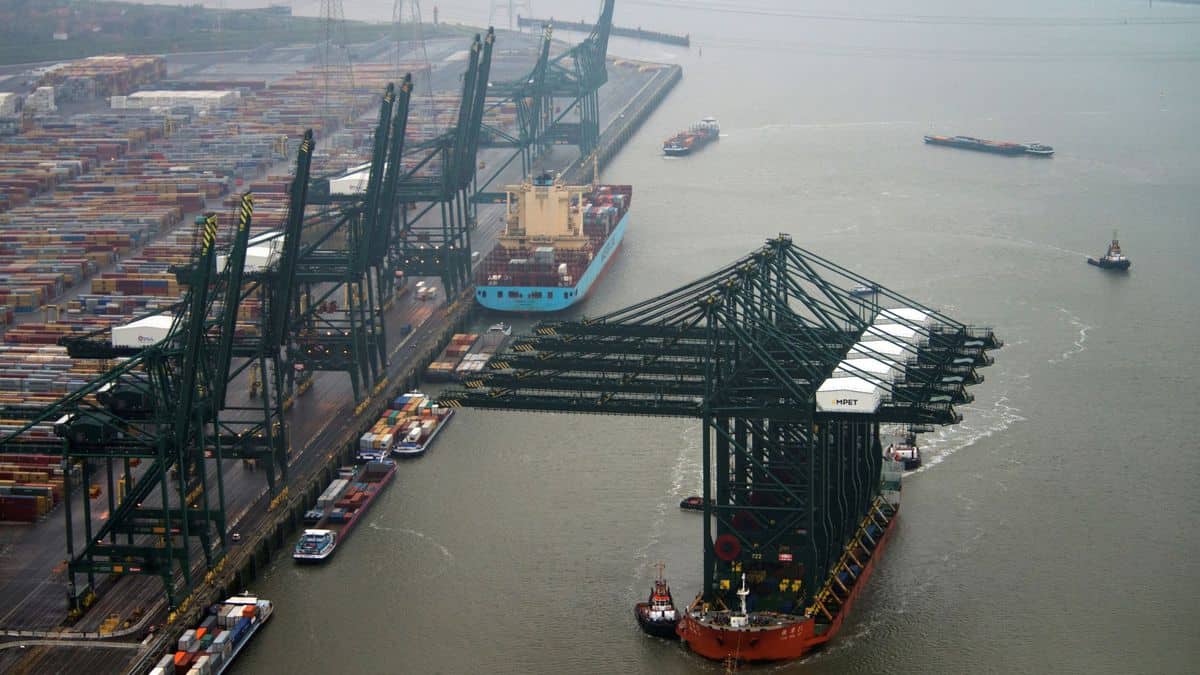 Aerial view of a a vessel tied up to wharf with big cranes while a special ship transports big ship cranes down the middle of a waterway.