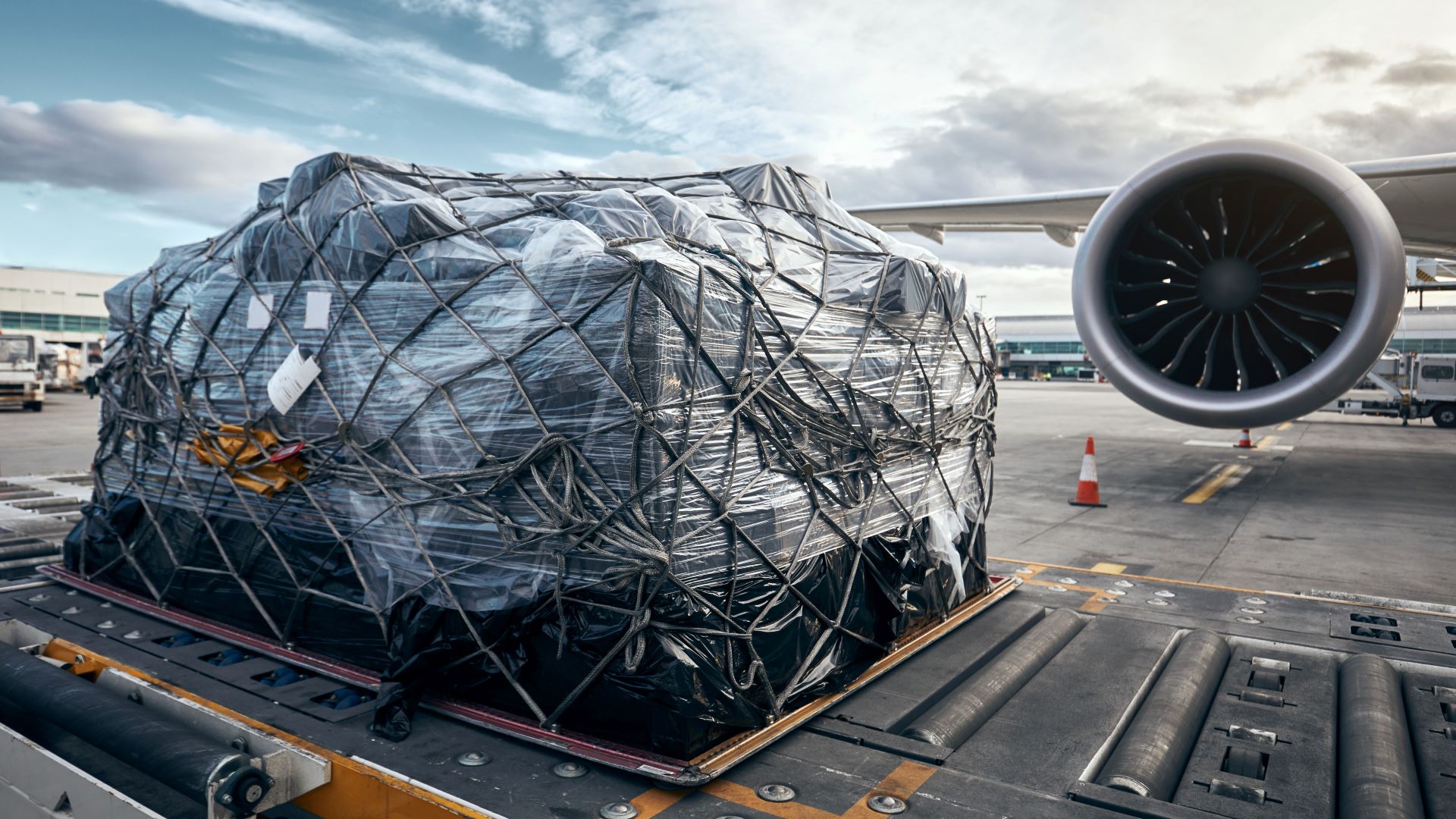 A large pallet with a tarp sits on a cart next to an airplane wing and engine.