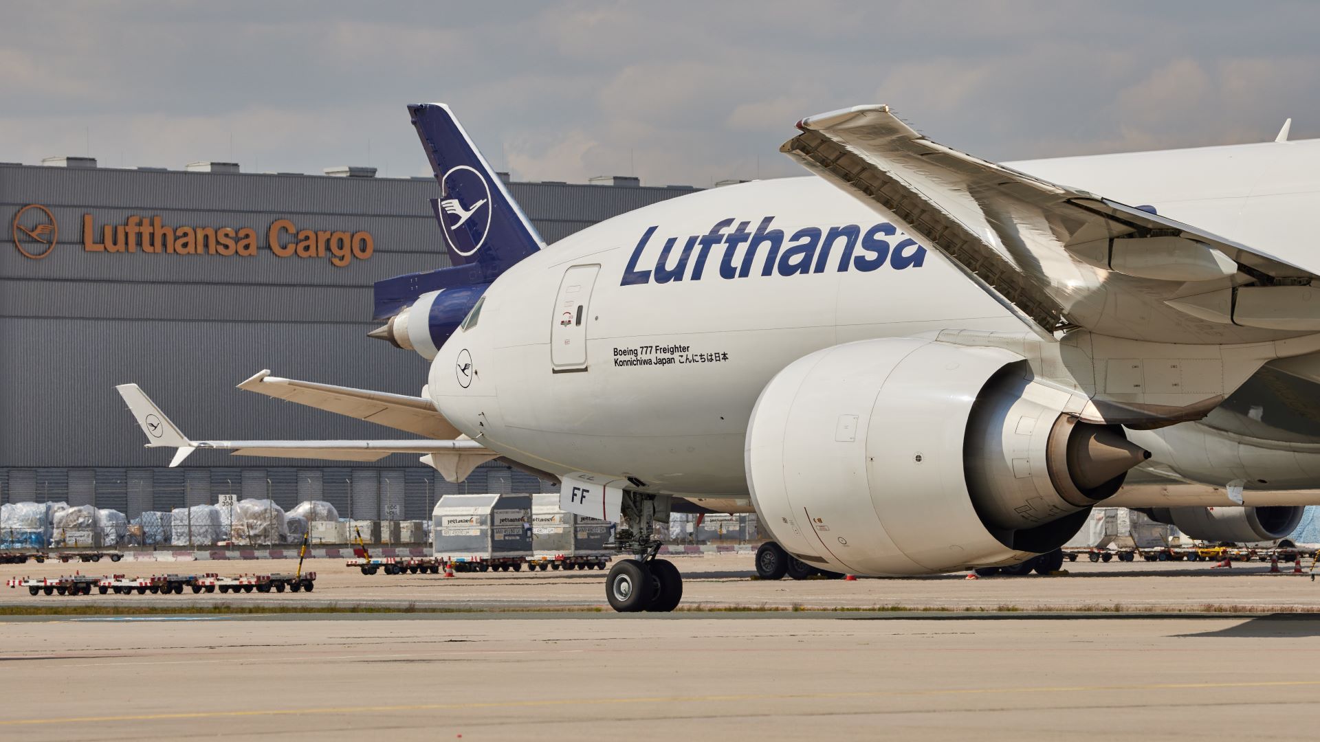 Partial view of a white Lufthansa plane in front of the cargo building.